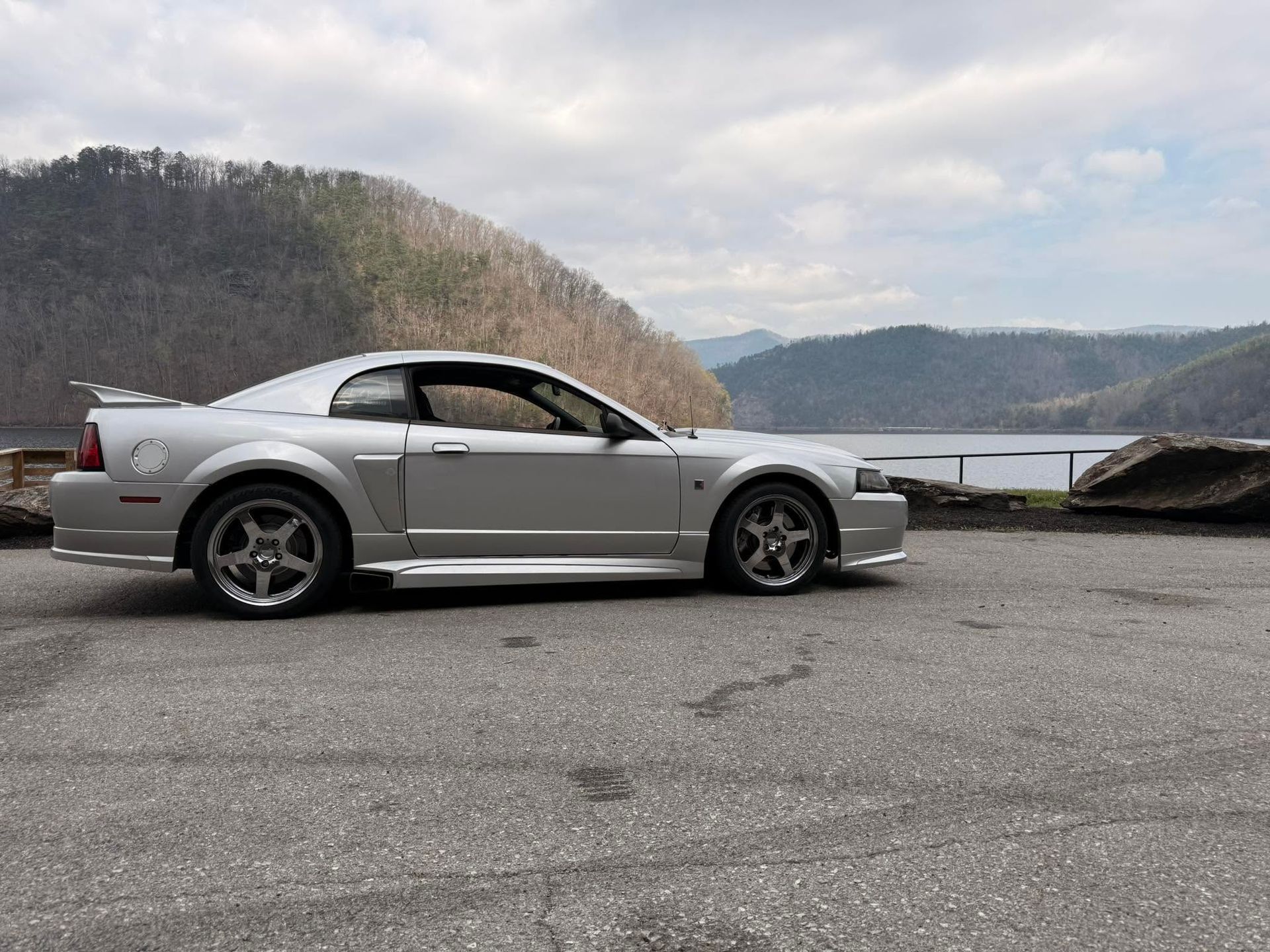 Silver sports coupe parked by a lakeside road with mountains in the background