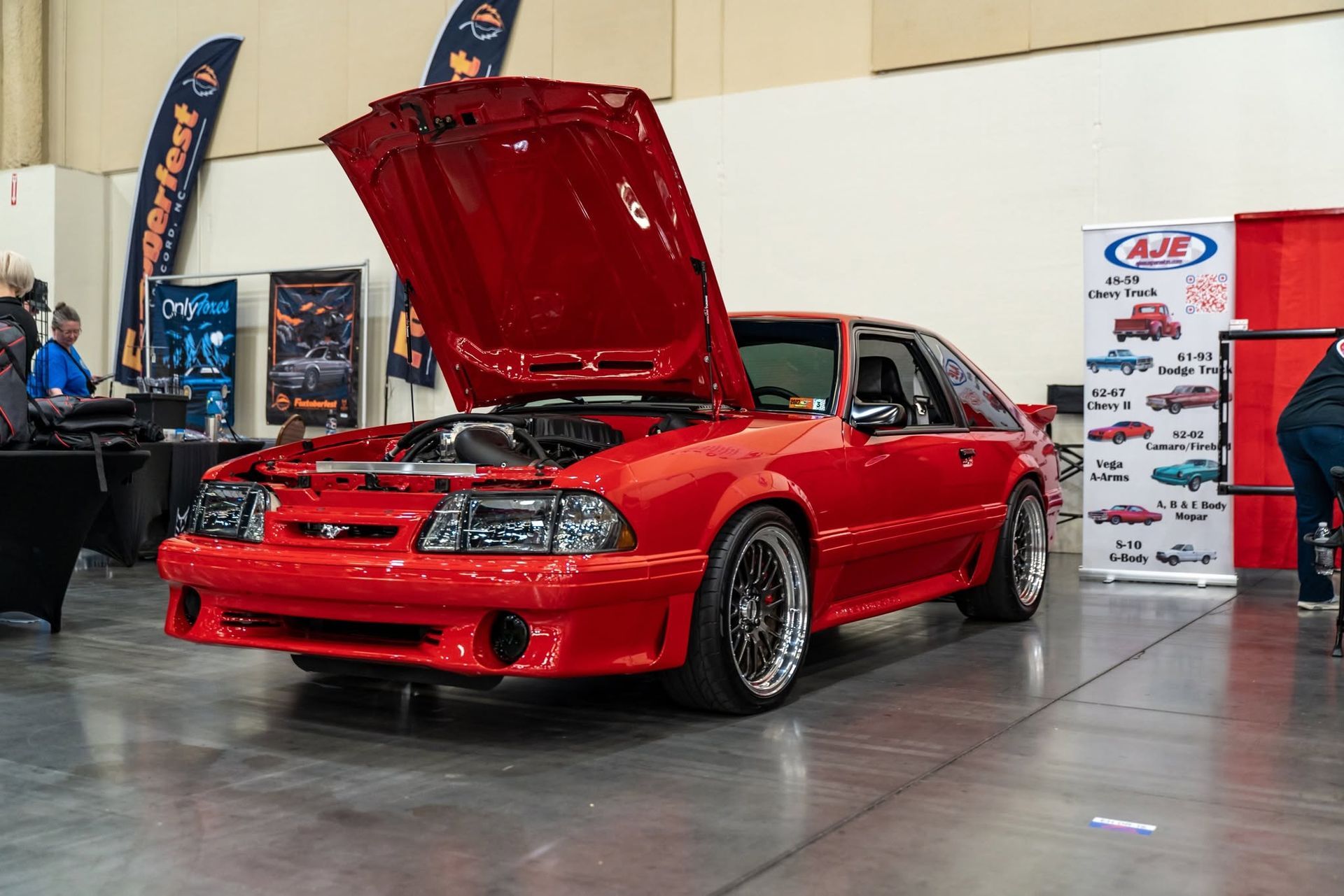 Red sports car with hood open on display at an indoor auto show