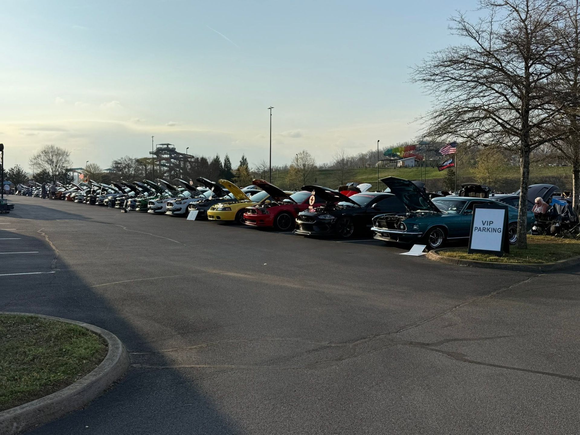 Long line of parked cars at an outdoor car show along a road at dusk