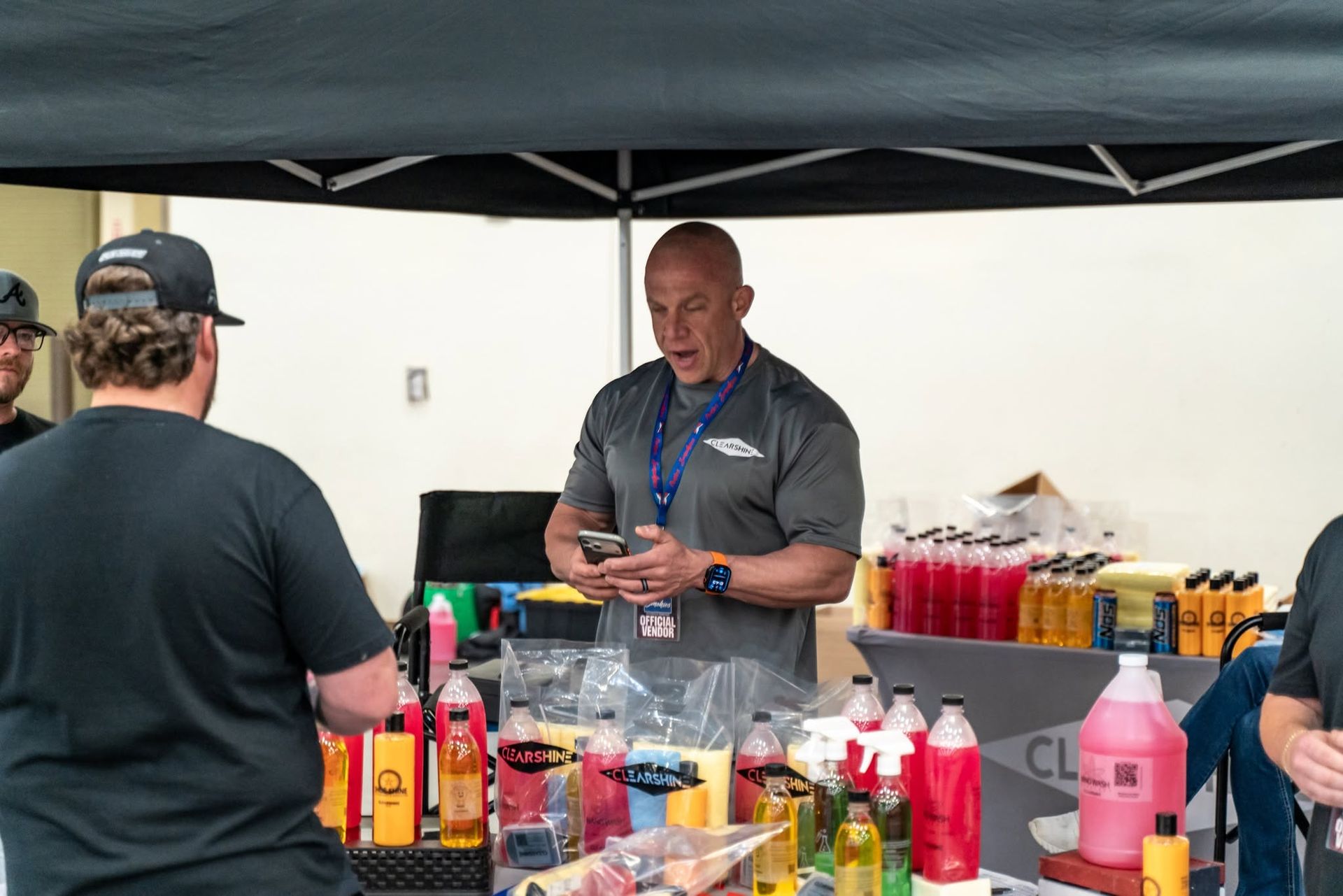 Vendor at outdoor booth with bottles of colorful drinks and condiments under a canopy