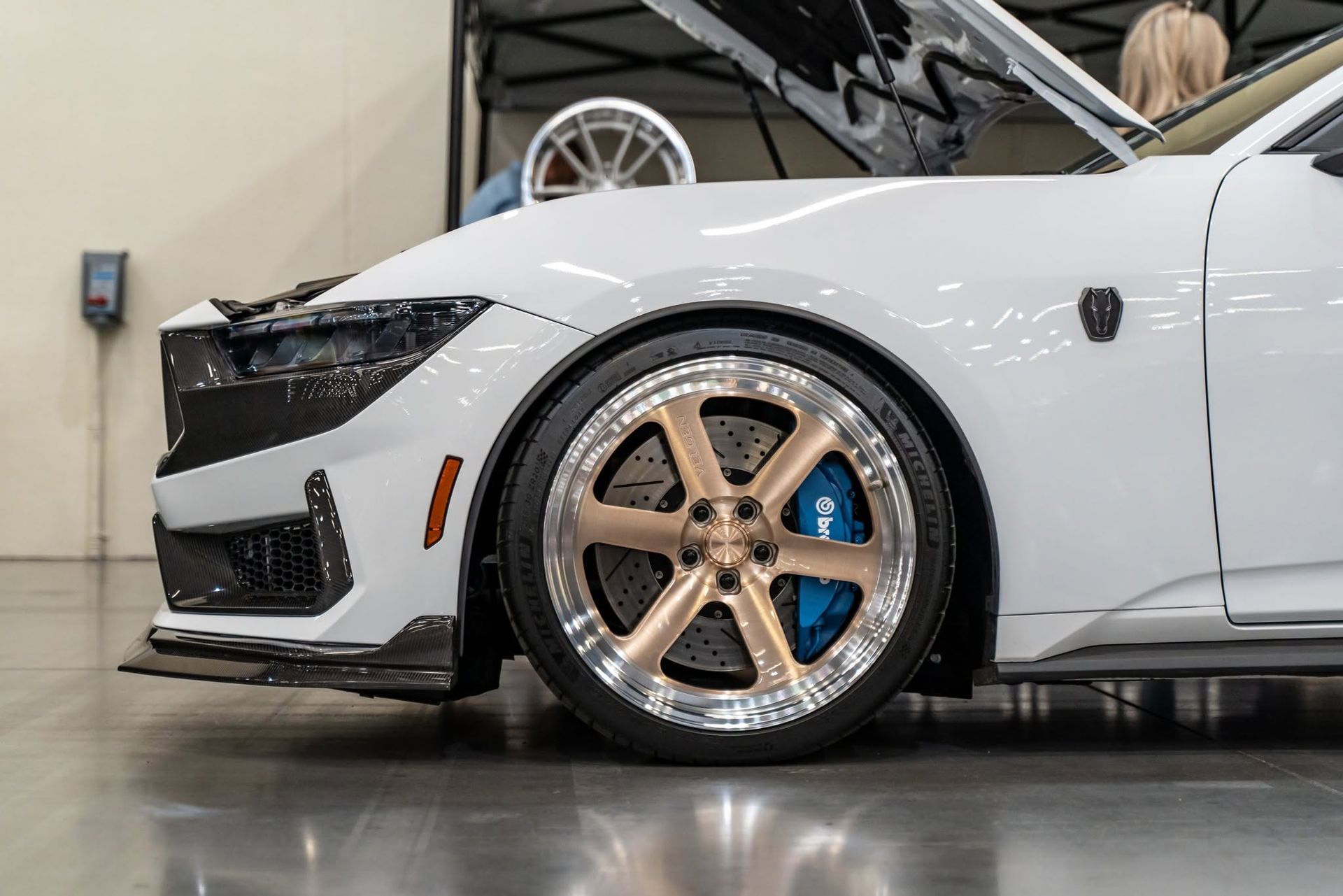 White modified sports car with bronze wheels in a showroom, side view