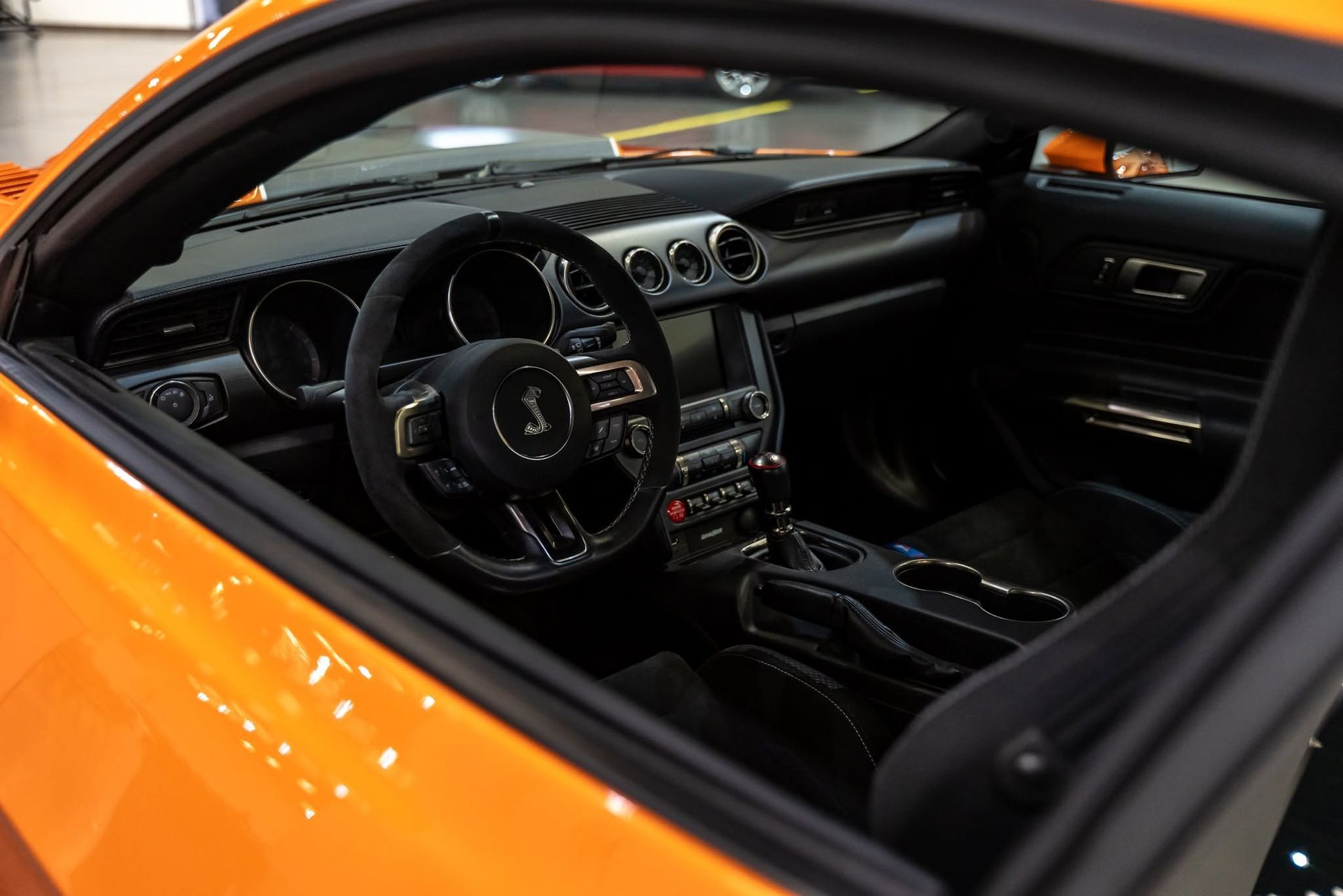 Orange sports car interior with black dashboard and steering wheel, viewed through the open window