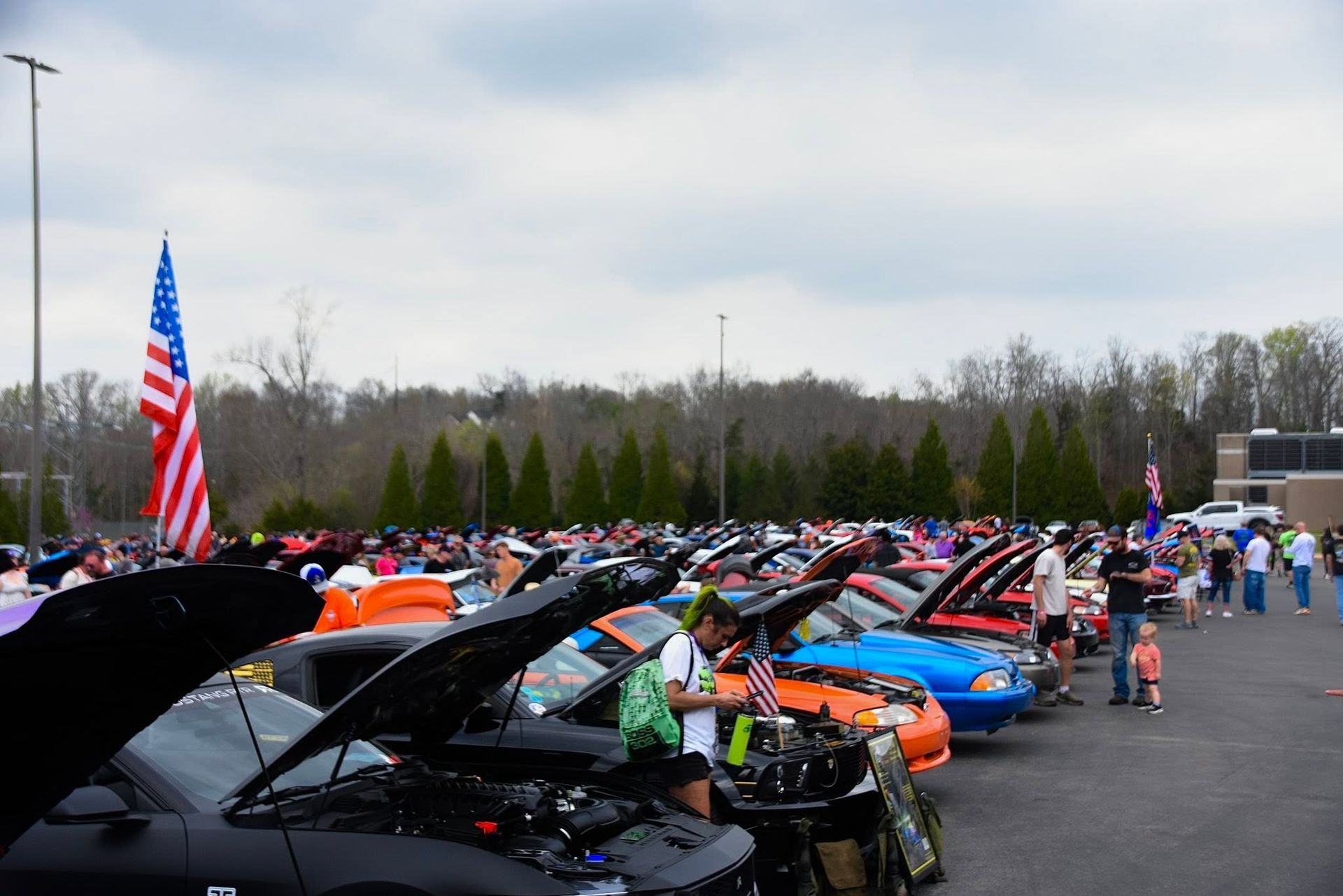 Classic car show with rows of open-hood sports cars and an American flag in a parking lot