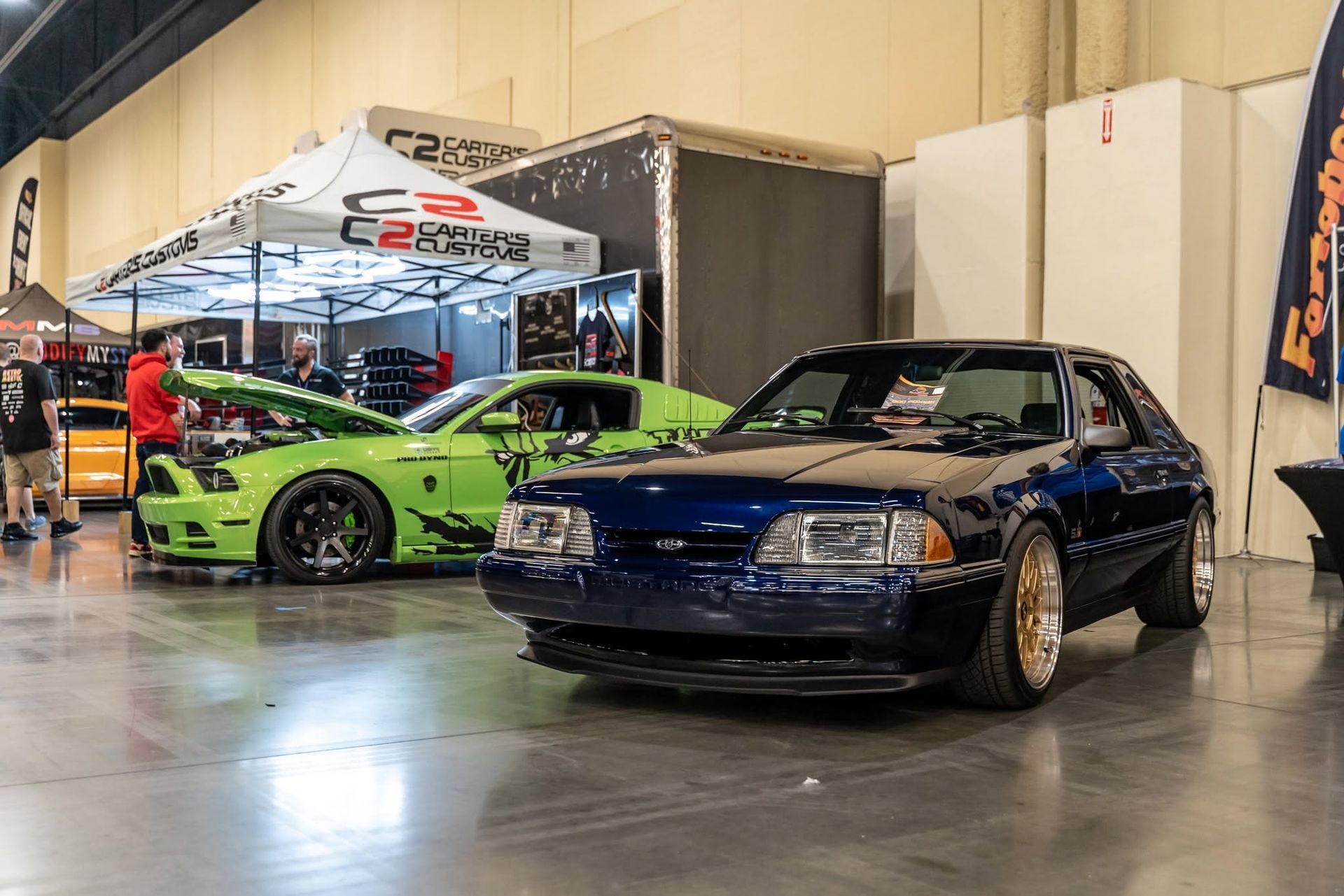 Blue and lime-green sports cars displayed at an indoor car show booth
