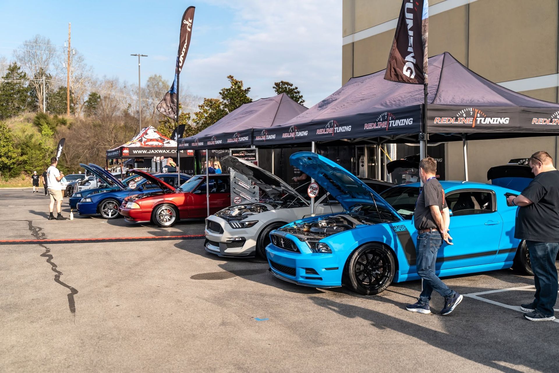 Sports cars displayed under tents at an outdoor car show, including a bright blue car with its hood open.