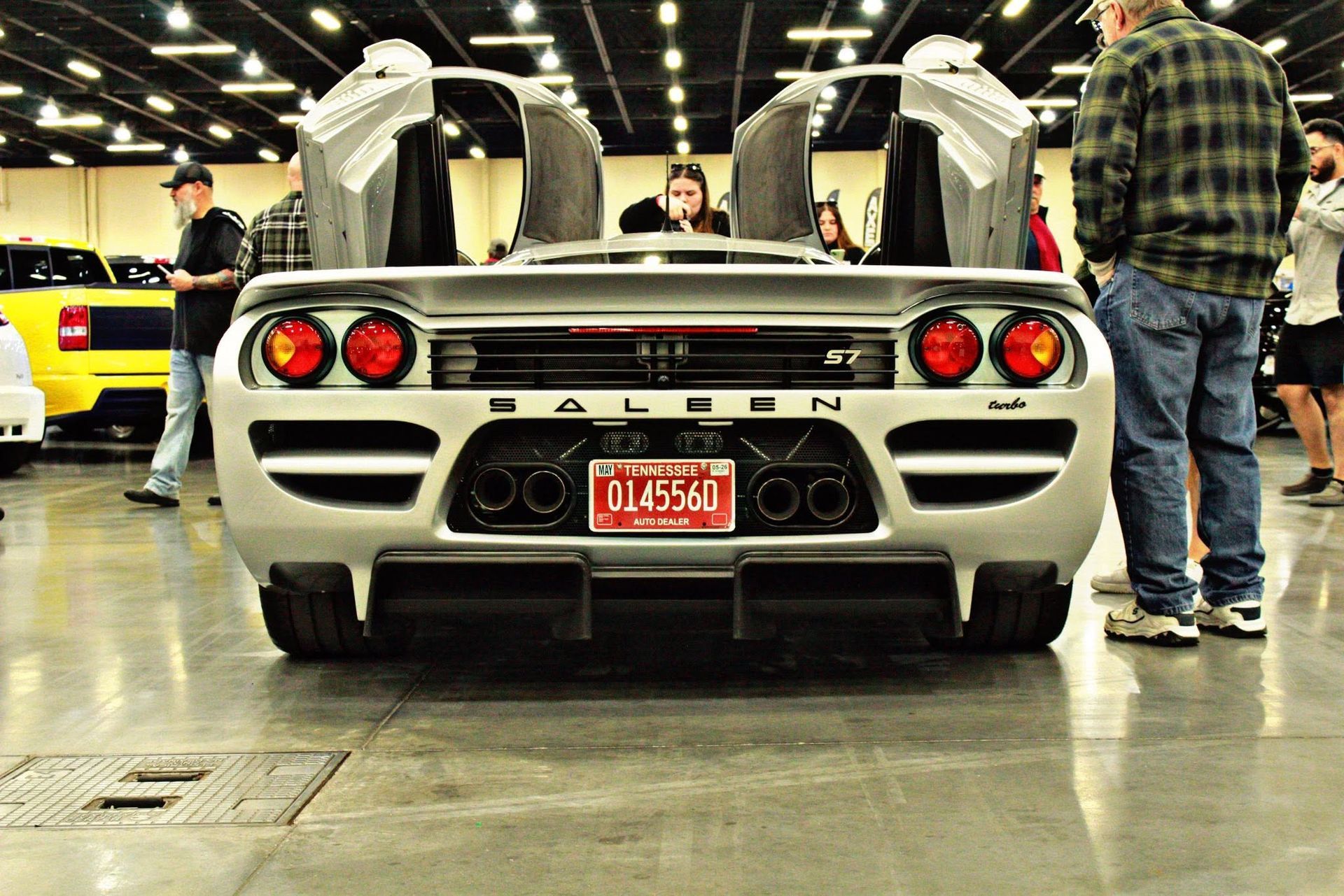 Rear view of a white sports car with raised doors at an indoor car show