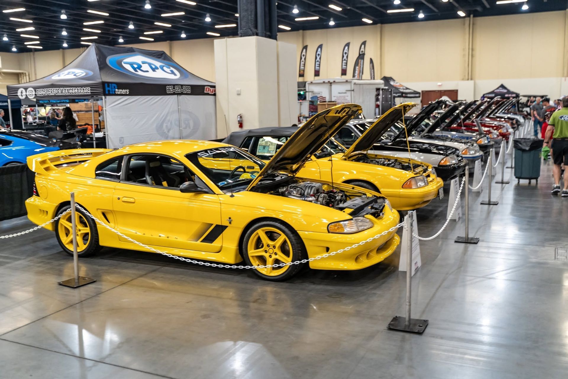 Yellow sports cars displayed at an auto show, one with its hood open