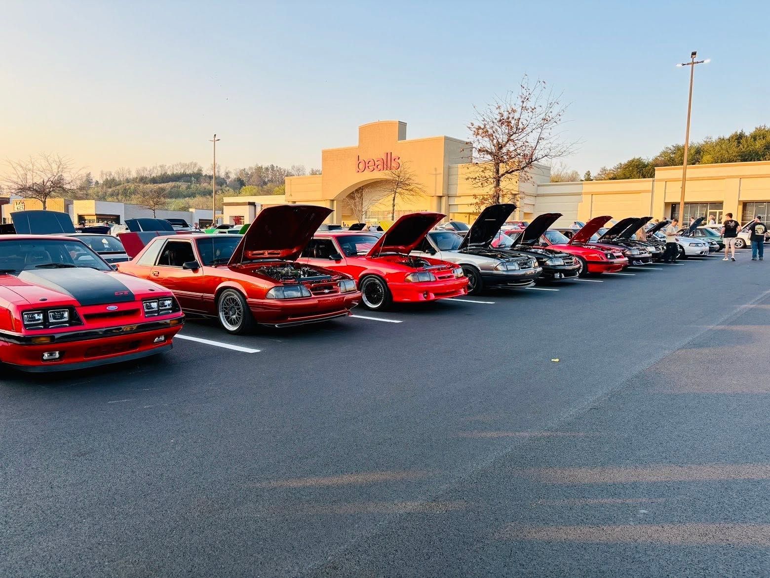 Line of red classic cars with hoods open in a parking lot at sunset
