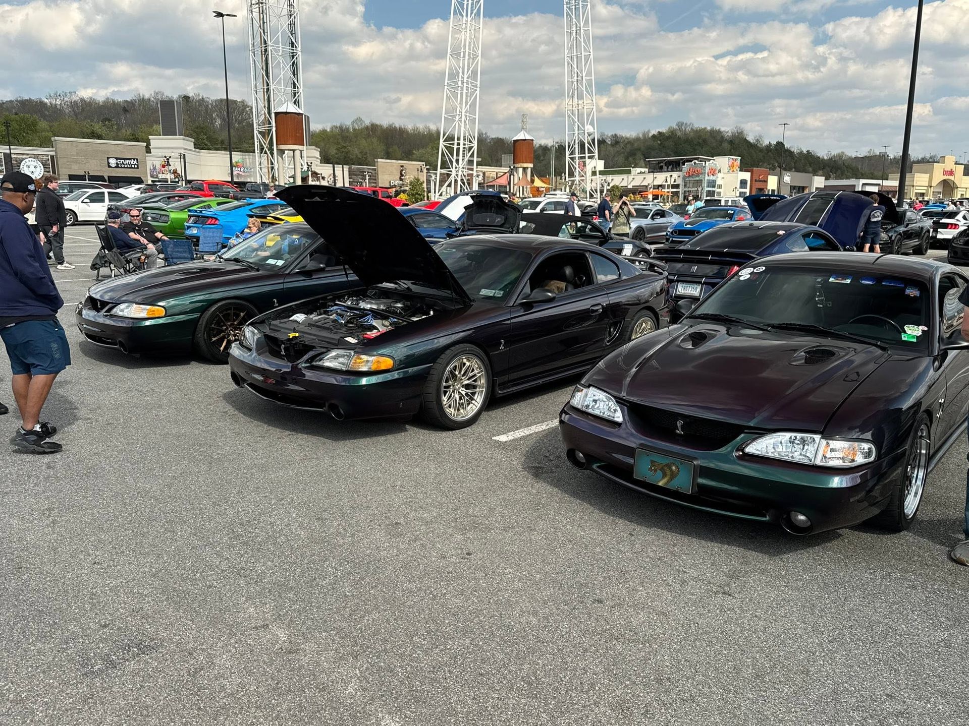 Cars lined up at a parking lot car show, including a black car with its hood open.