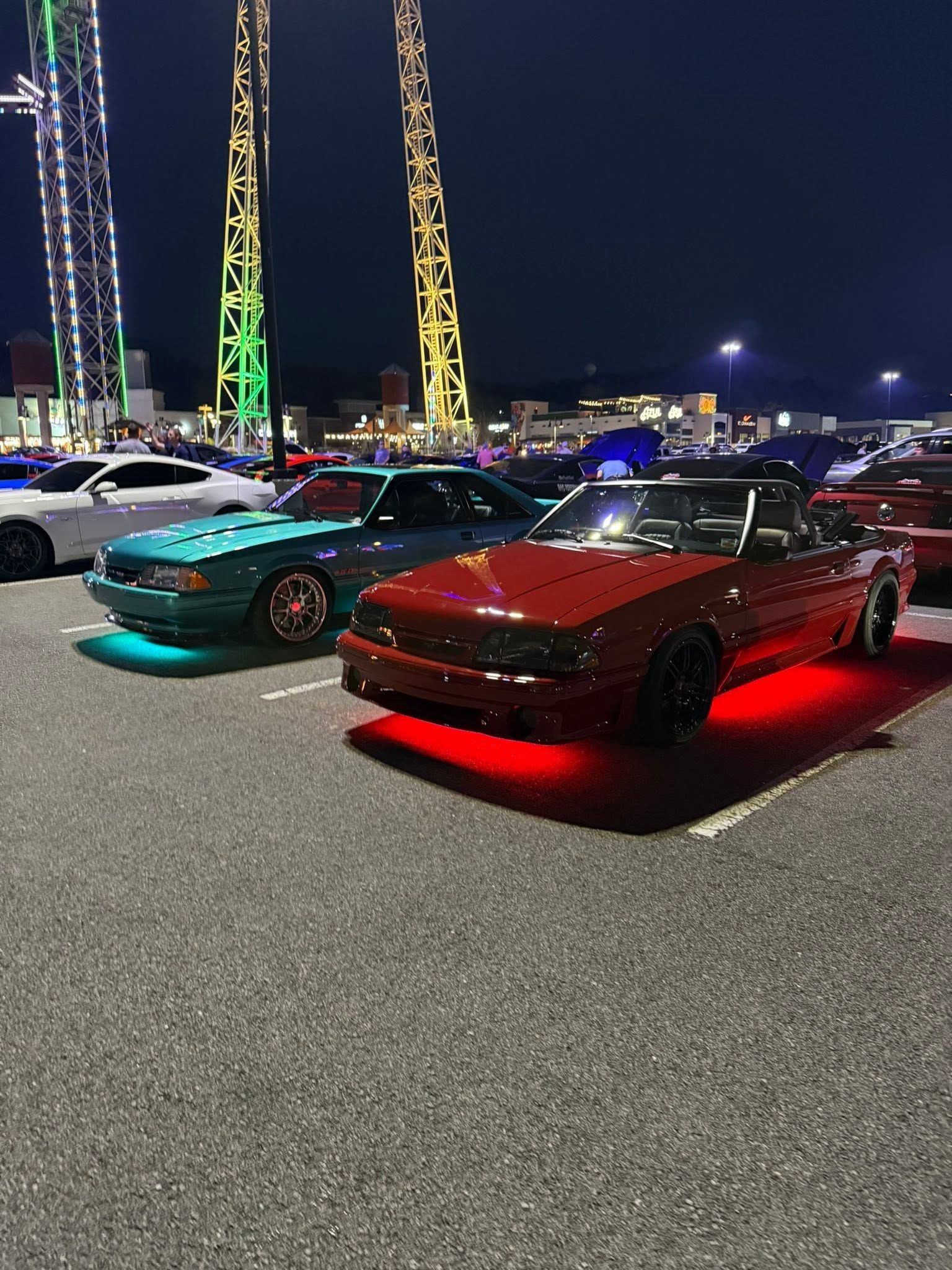 Modified cars parked at night, including a red car with glowing red underbody lights.
