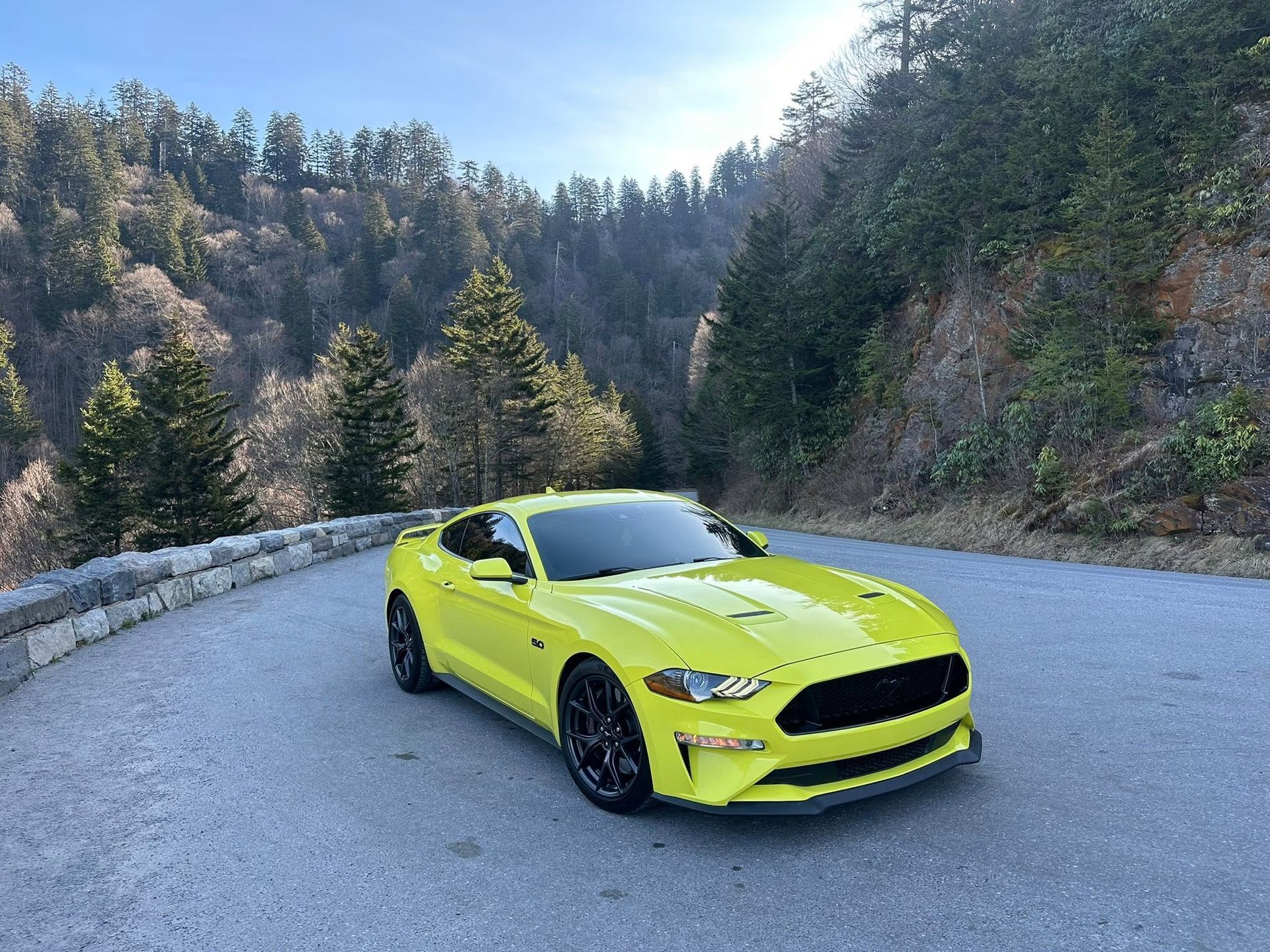 Bright lime sports car on a mountain road with trees and cliffs around it