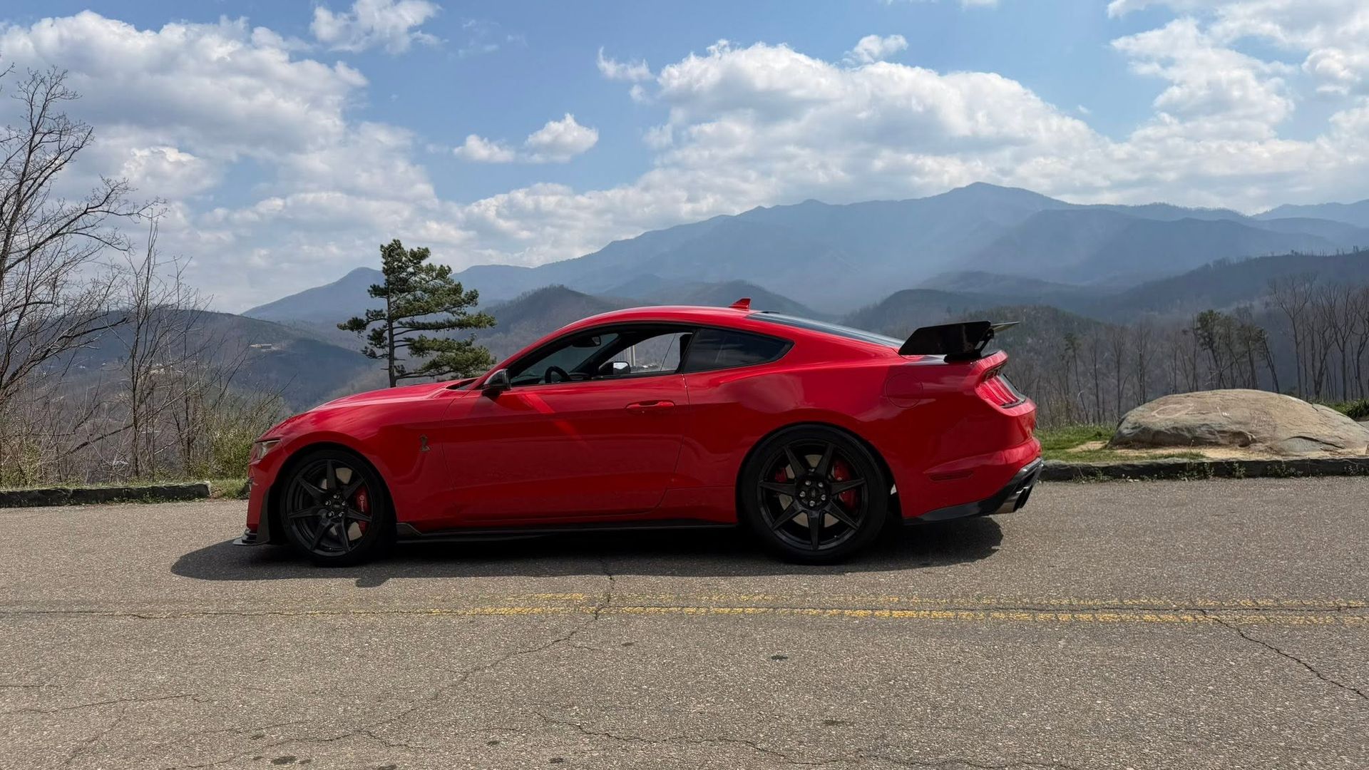 Red sports coupe parked on a roadside with mountains and cloudy sky in the background