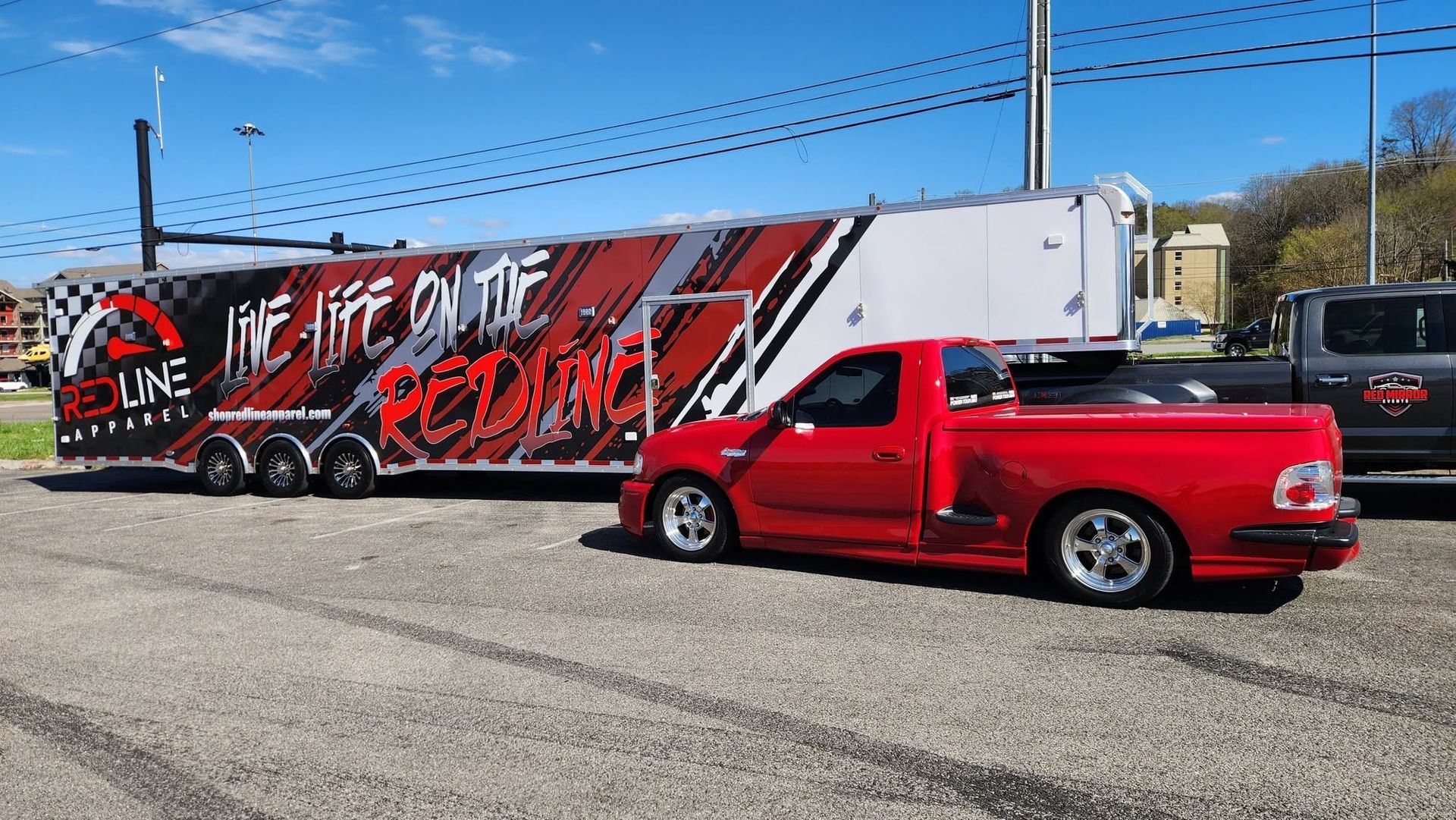 Red lowered pickup truck towing a red-and-black race trailer on a sunny roadside.