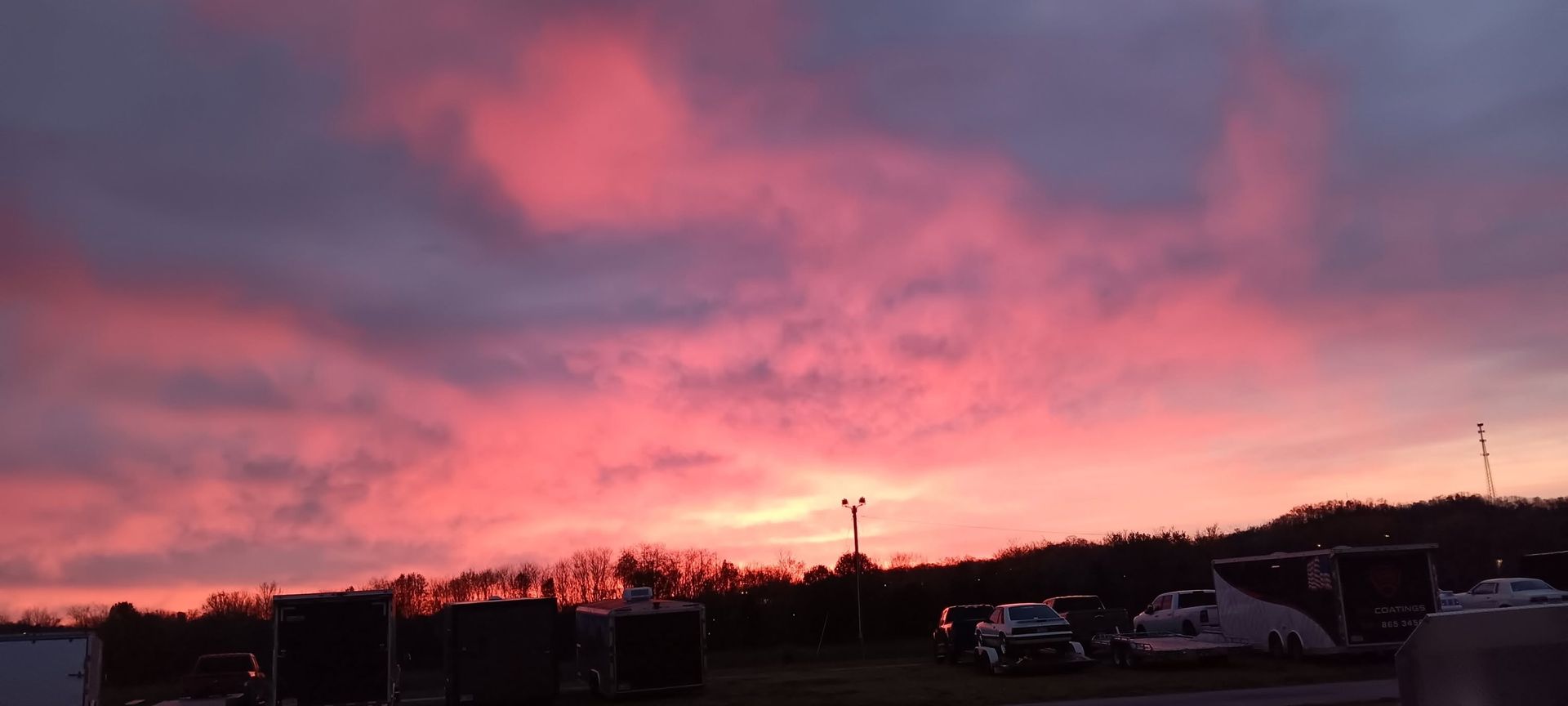 Pink sunset sky over a parking lot with silhouetted cars and buildings.