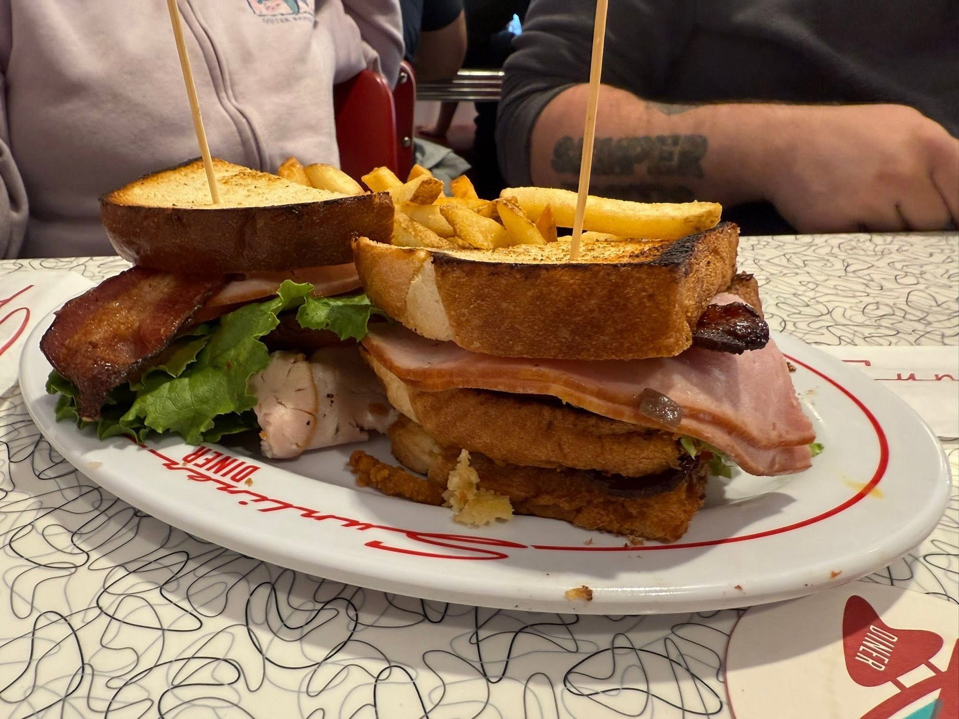 Stacked sandwich with toasted bread and fries on a plate at a restaurant table