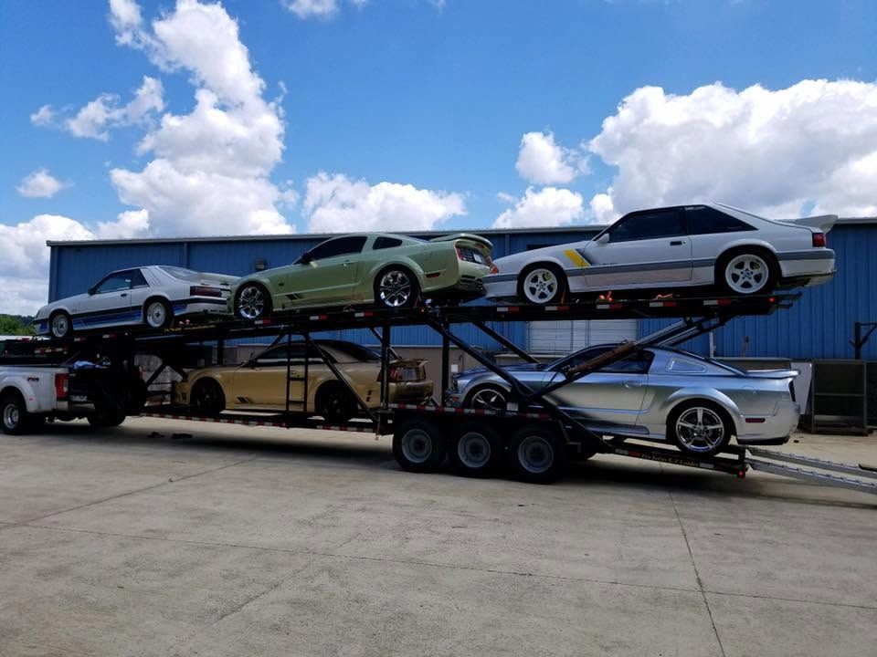 Three sports cars loaded on a multi-level car carrier truck under a blue sky