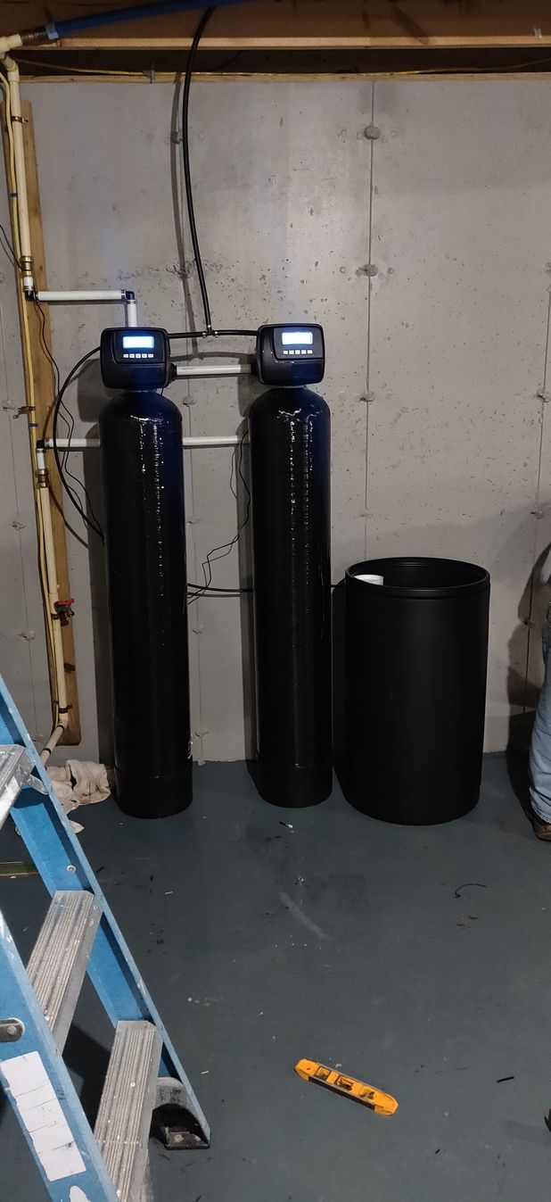 Two water softeners are sitting in a room next to a ladder.