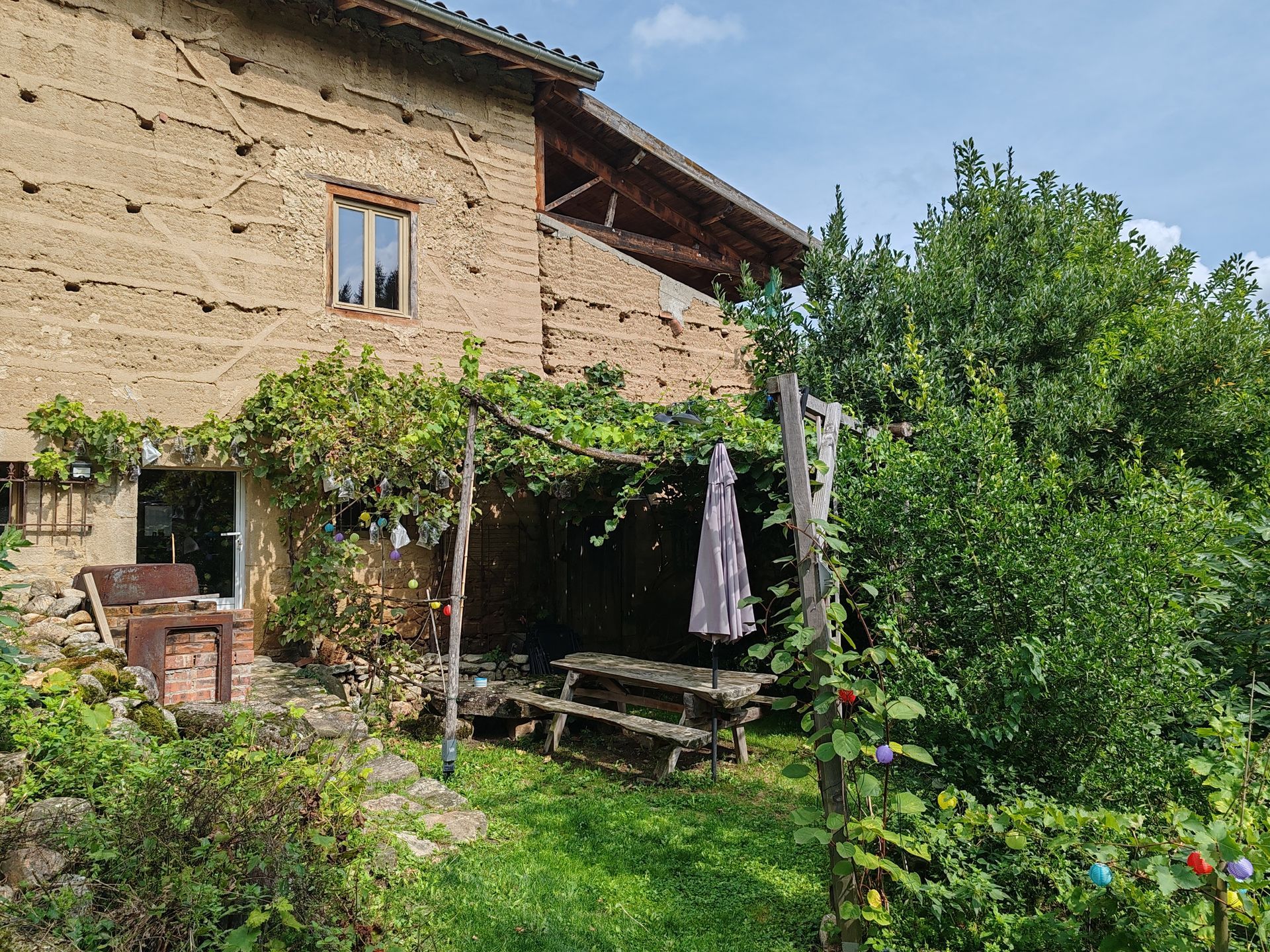 Façade de maison en pisé, table BBQ et parasol 