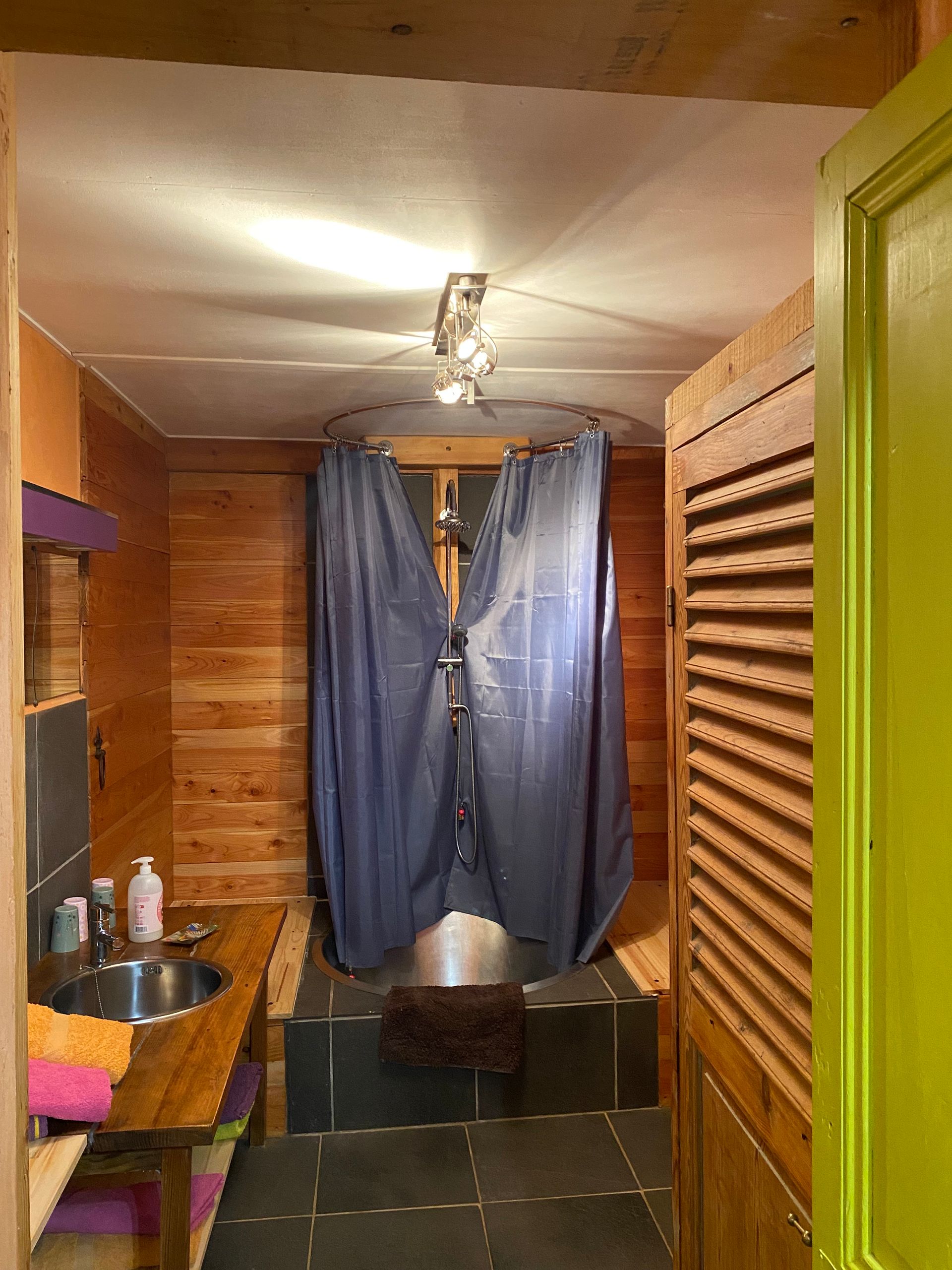 Salle de bain avec murs lambrissés, rideau de douche circulaire et lavabo sur plan de travail en bois. 
