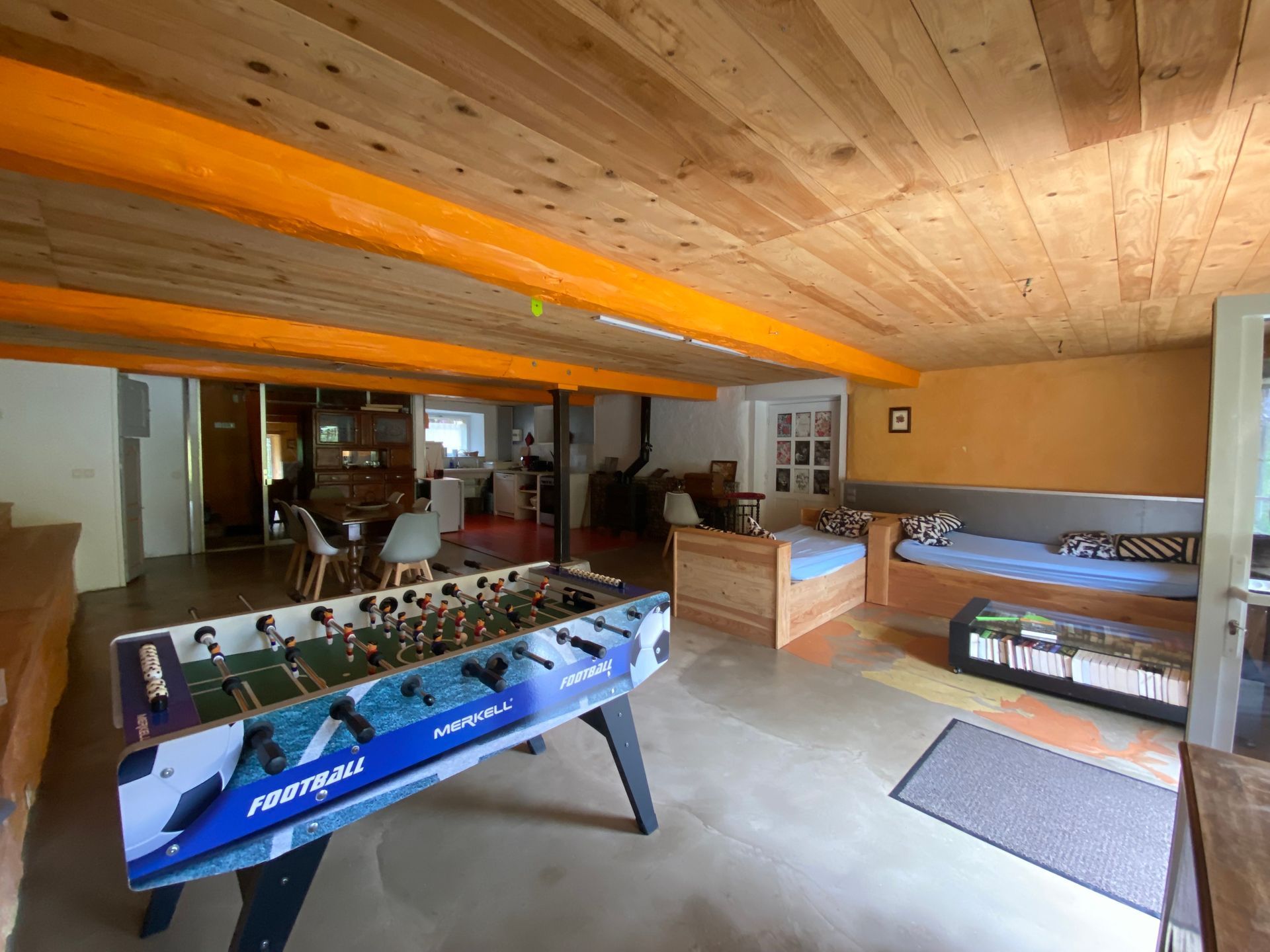 Une salle de loisirs rustique avec une table de baby-foot, des lits de repos et des poutres en bois au plafond.