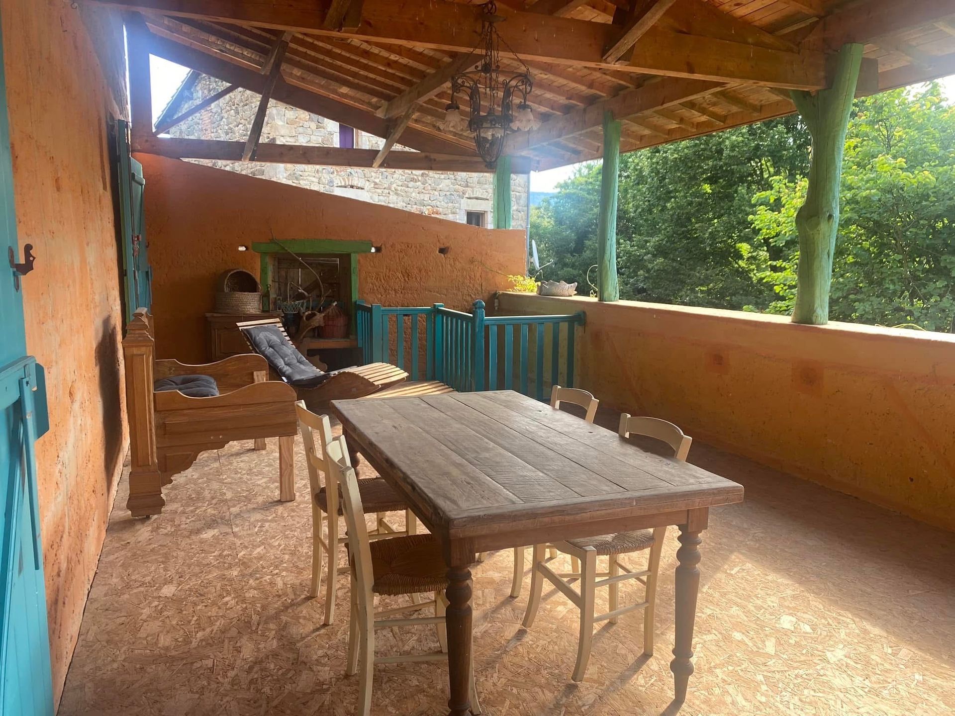 Espace repas extérieur avec une table et des chaises en bois sur une terrasse avec un mur orange et un toit à baldaquin.