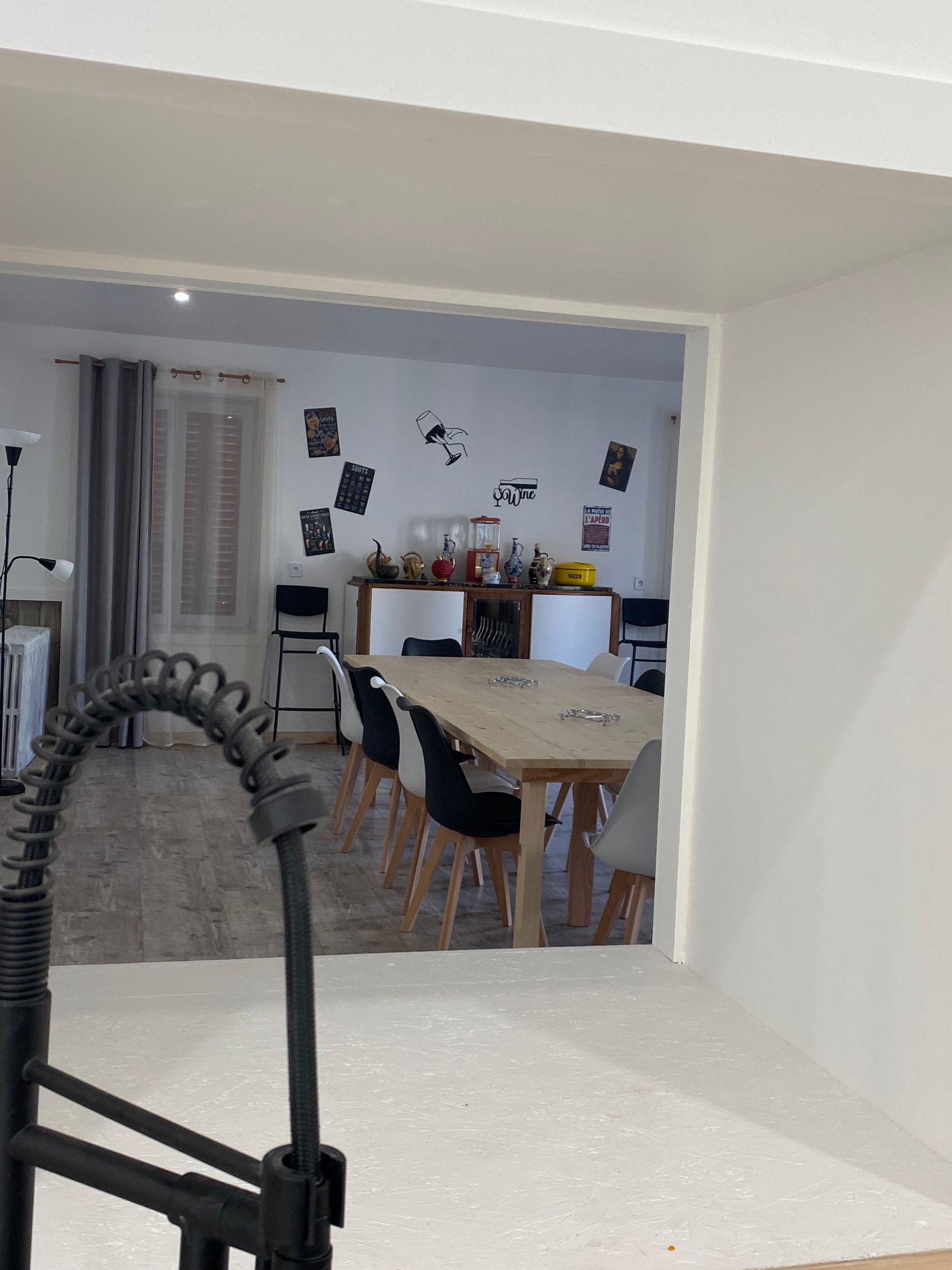 Porte ouverte sur la salle à manger avec une longue table en bois, des chaises et un bar contre le mur décoré d'affiches.