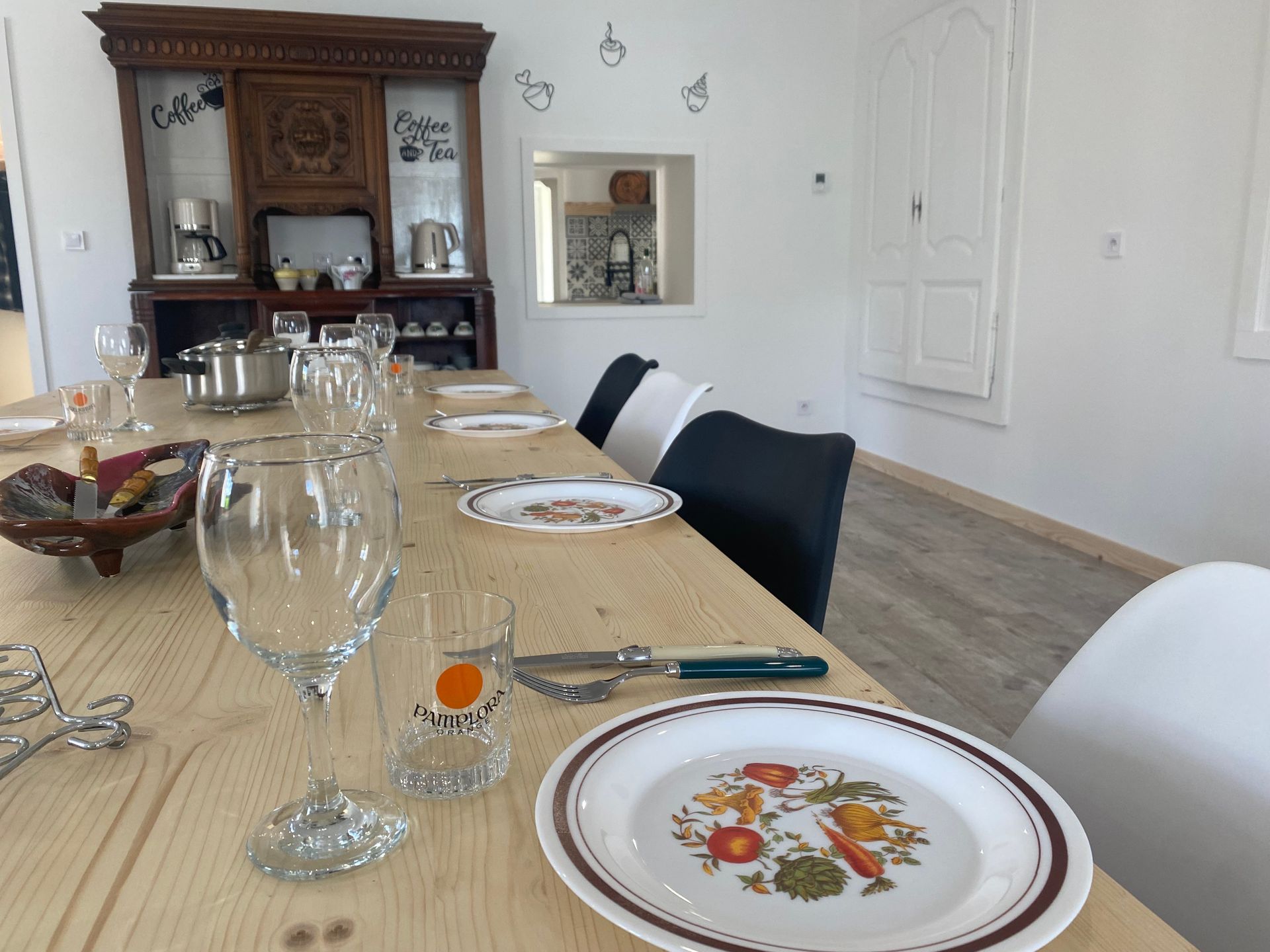 Une longue table à manger en bois est dressée pour un repas, avec assiettes, verres et couverts.