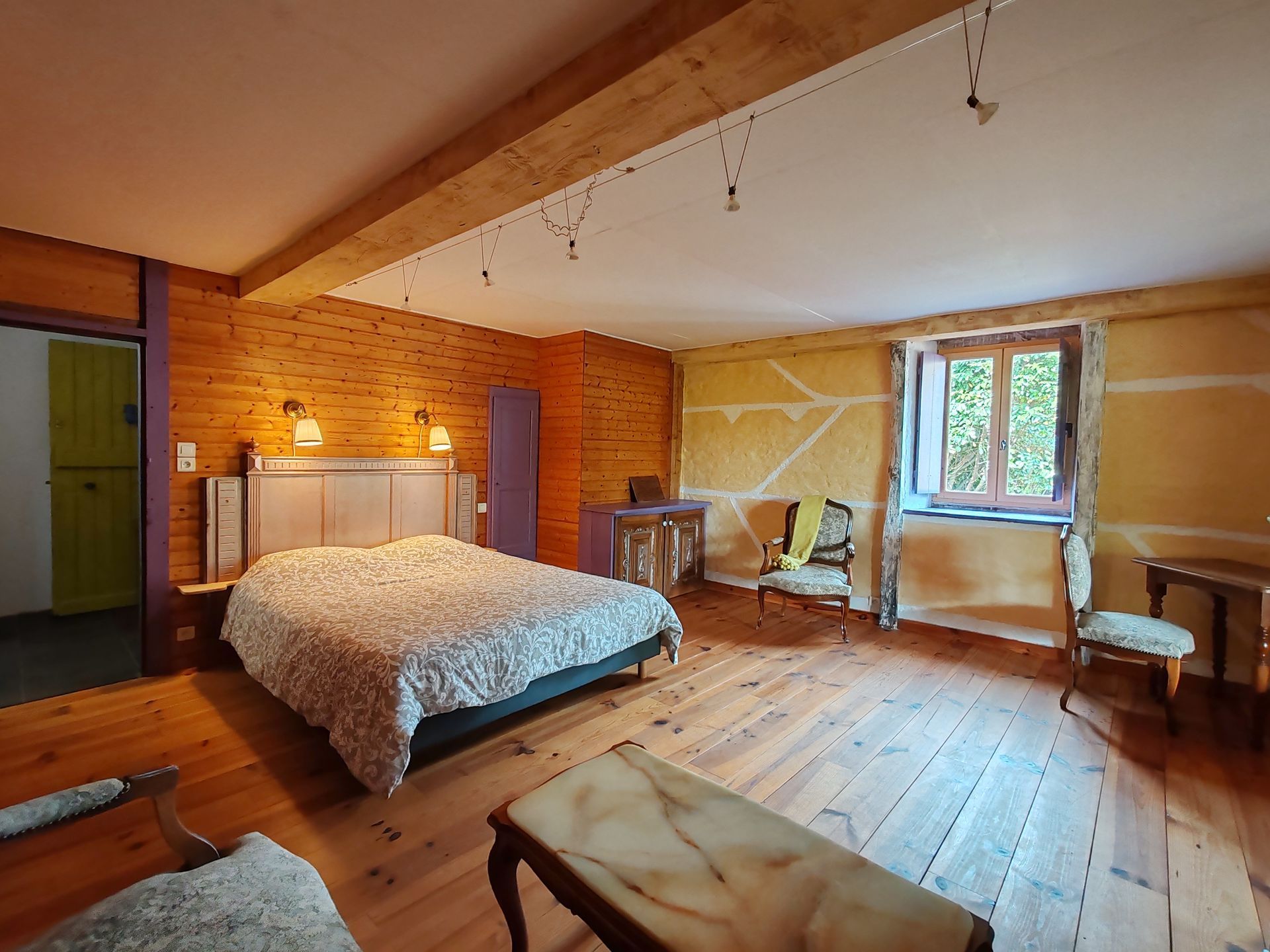 chambre au parquet de bois huilé, fauteuil d'époque, d'un lit couvert d'une couette, petit bureau d'époque en bois foncé 