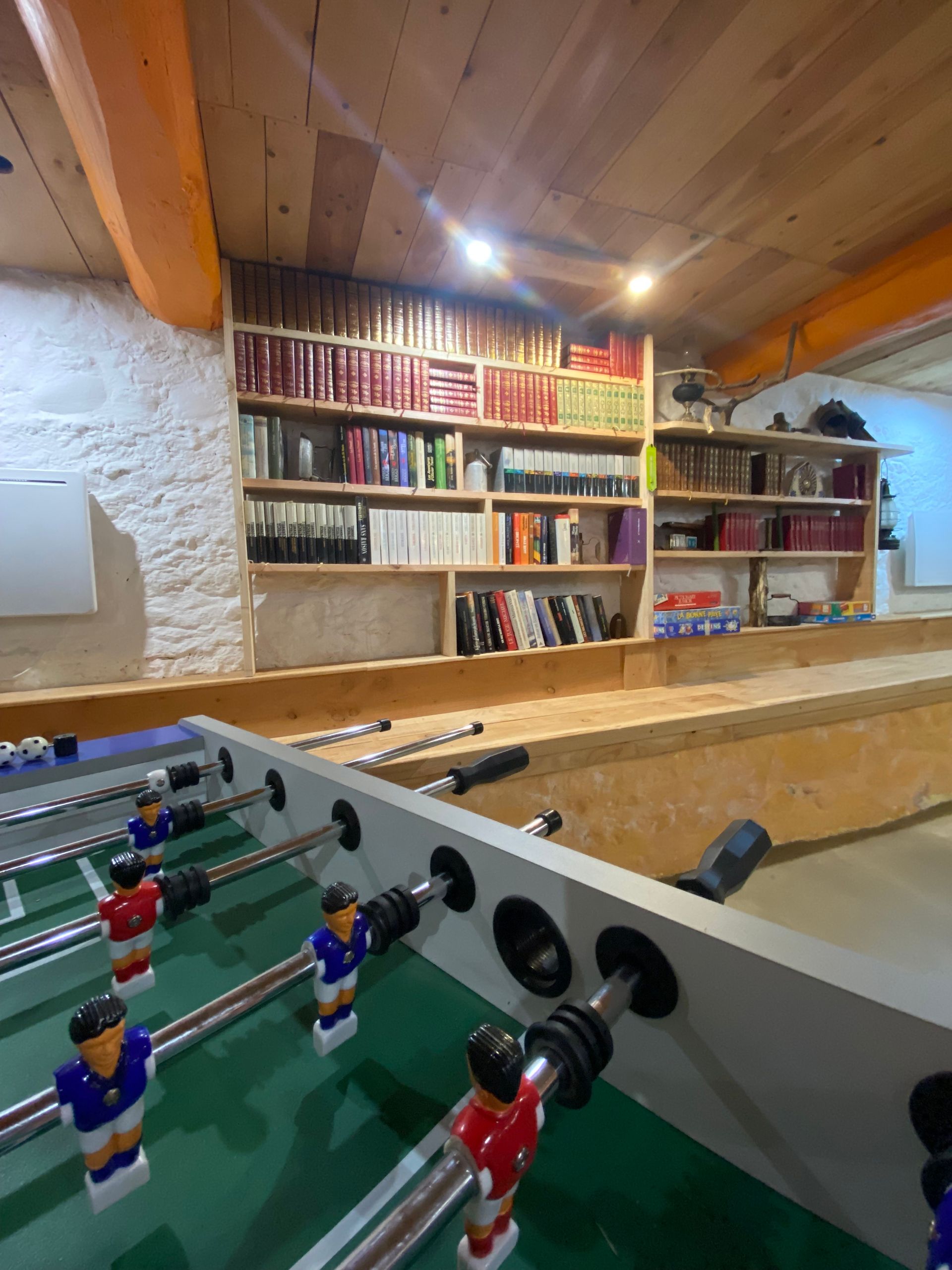bibliothéque dans un salon, décoré de vieux sabots, de lampe et de livres, des jeux saont aussi installé de ci de là