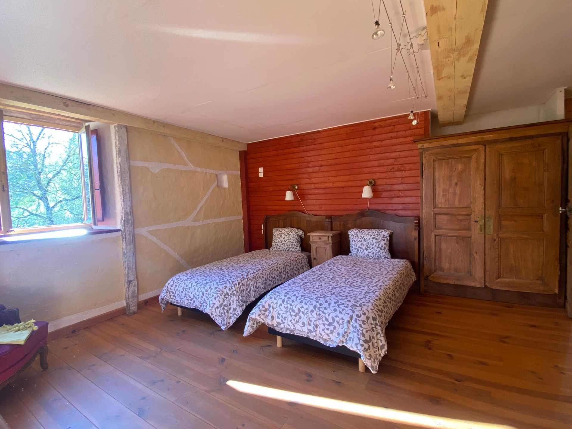 Chambre avec parquet et murs en bois, comprenant 2  lits et une table de nuit, un canapé, un fauteuil .