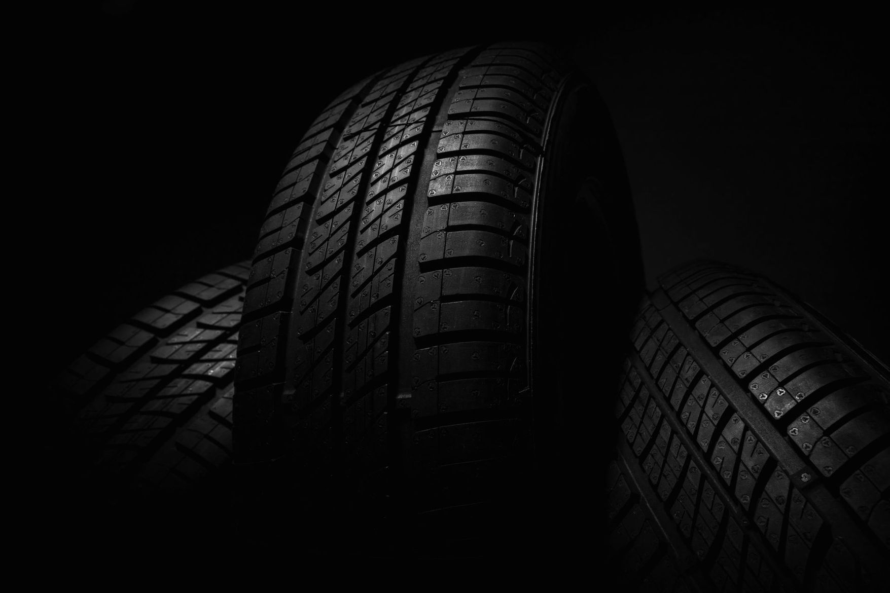 Tres neumáticos de coche sobre un fondo negro oscuro, iluminados dramáticamente desde arriba.