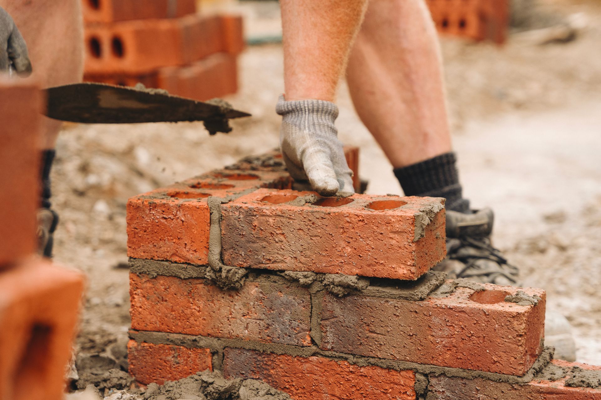Bricklayer laying bricks with mortar. Close-up on hands, brick wall in progress.