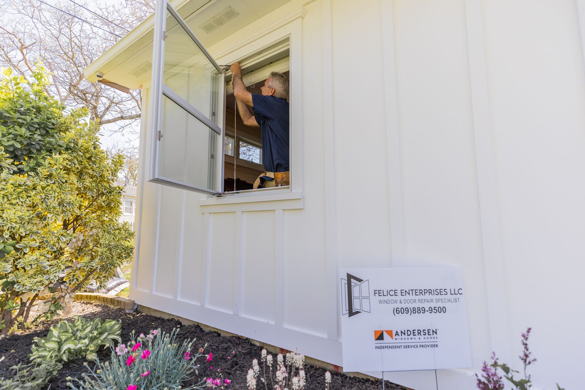 A man is fixing a window on a white house.