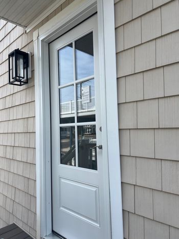 White exterior door with glass panes and wall-mounted lantern on a shingled house exterior