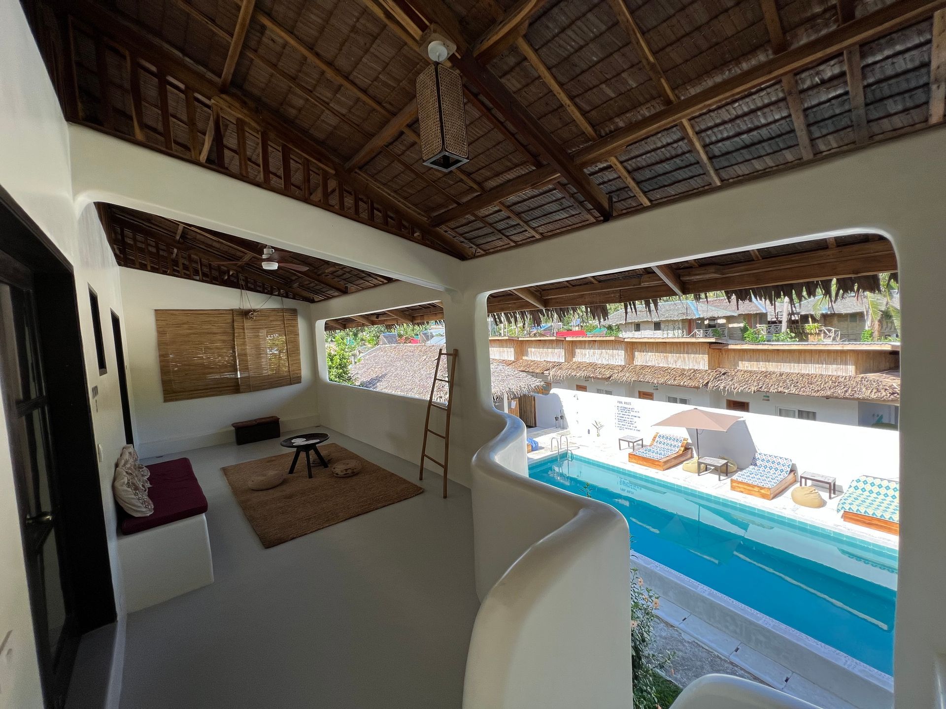 A living room with a thatched roof and a swimming pool in the background.