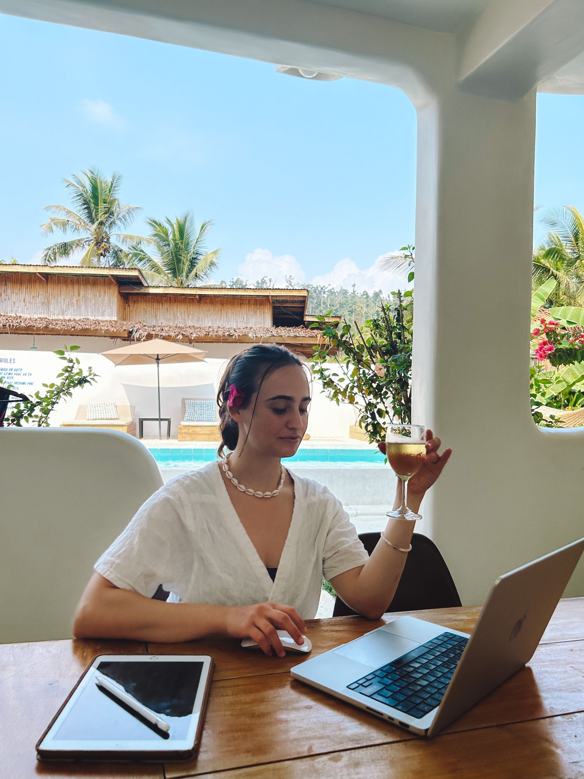 A woman is sitting at a table with a laptop and a glass of wine.