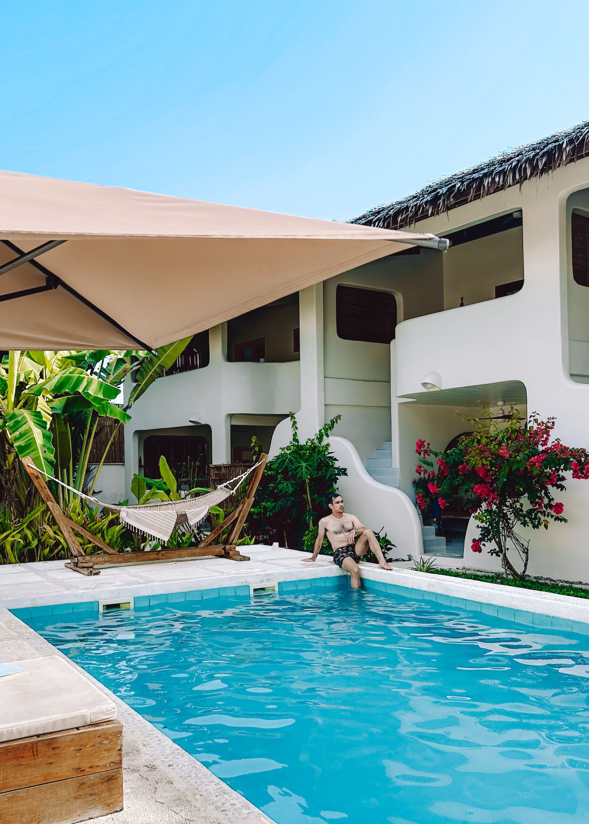 A man is sitting in a swimming pool under an umbrella.