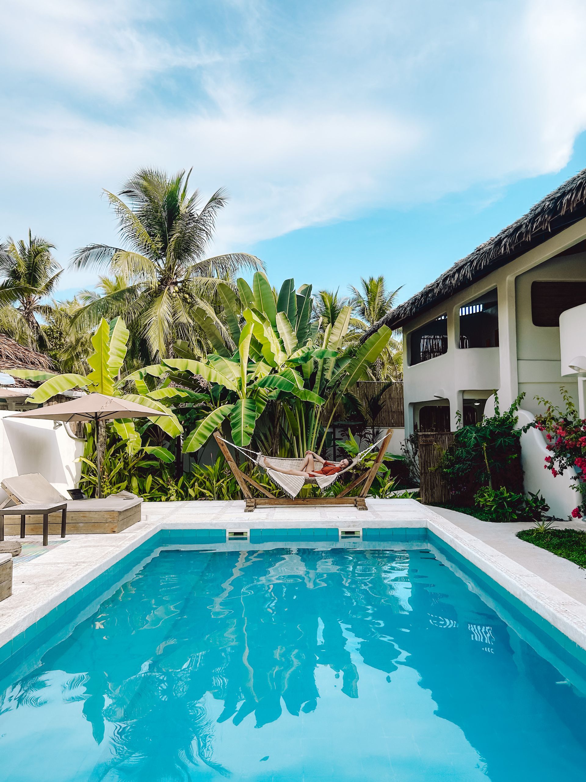 A large swimming pool surrounded by palm trees and a house.