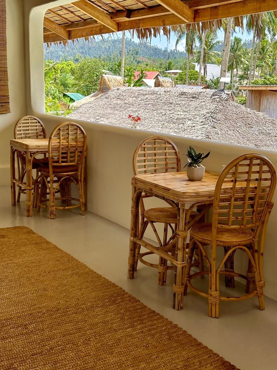 A wicker table and chairs on a balcony with a thatched roof.