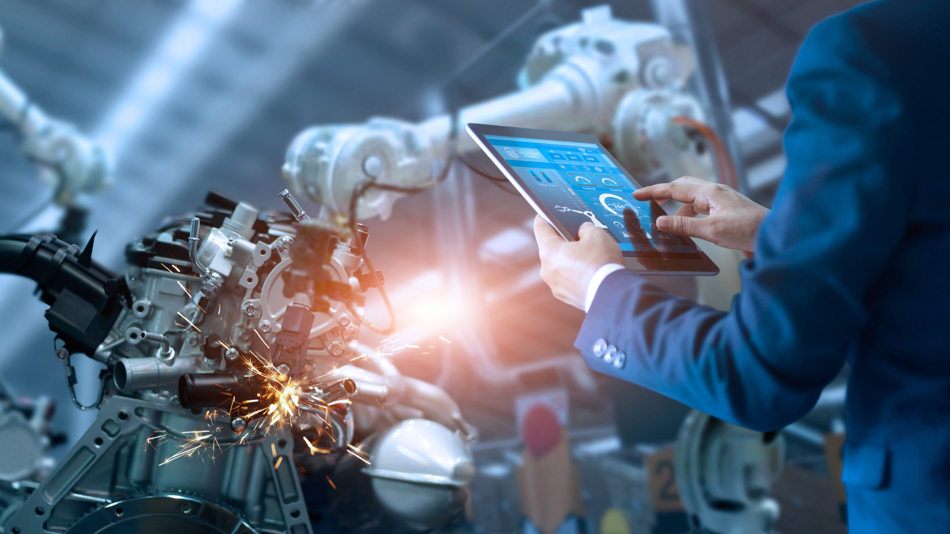 A man is holding a tablet in front of a robotic arm in a factory.