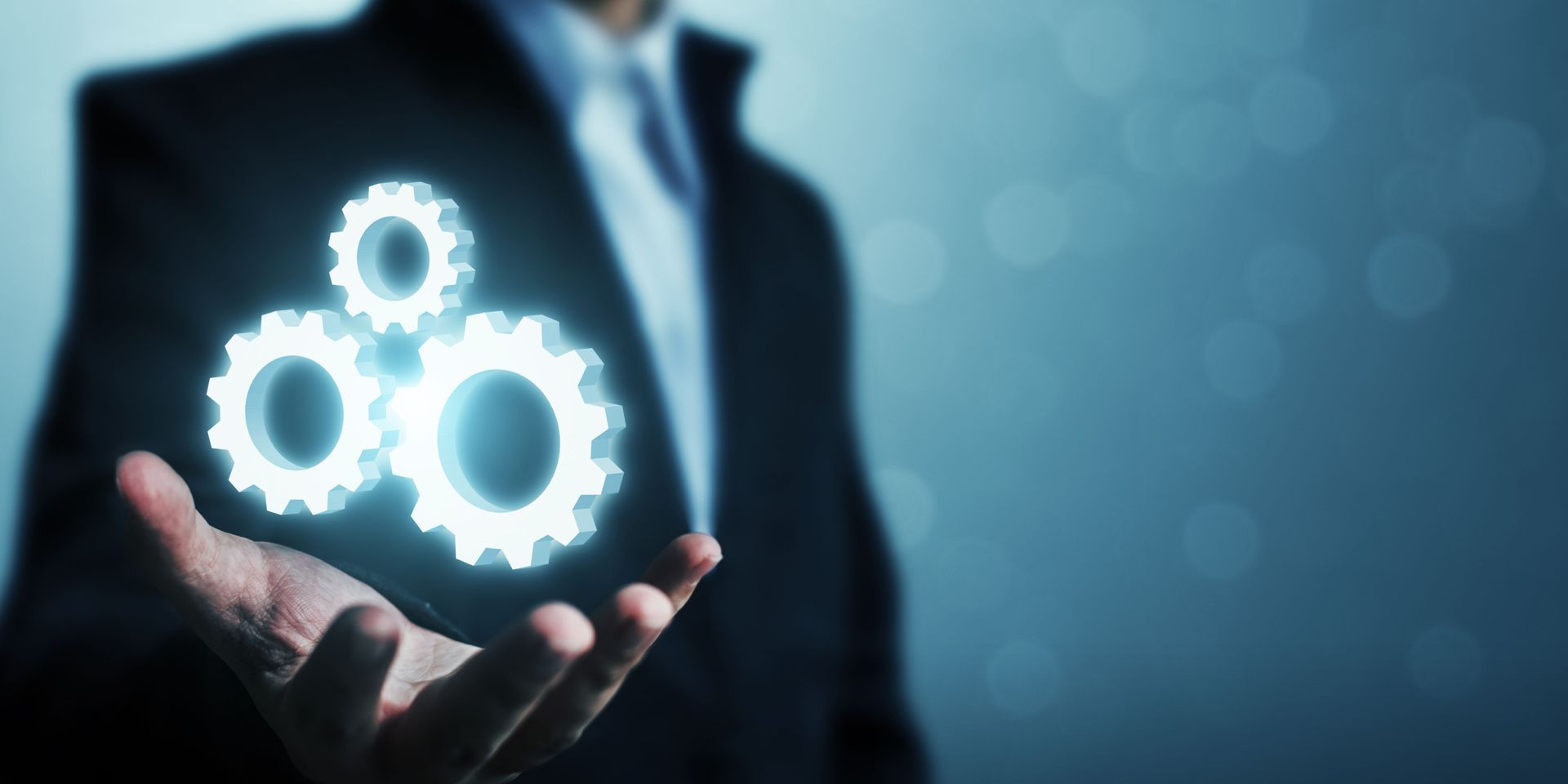 A man in a suit is holding three gears in his hand.