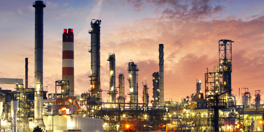 A large oil refinery is lit up at night with a sunset in the background.