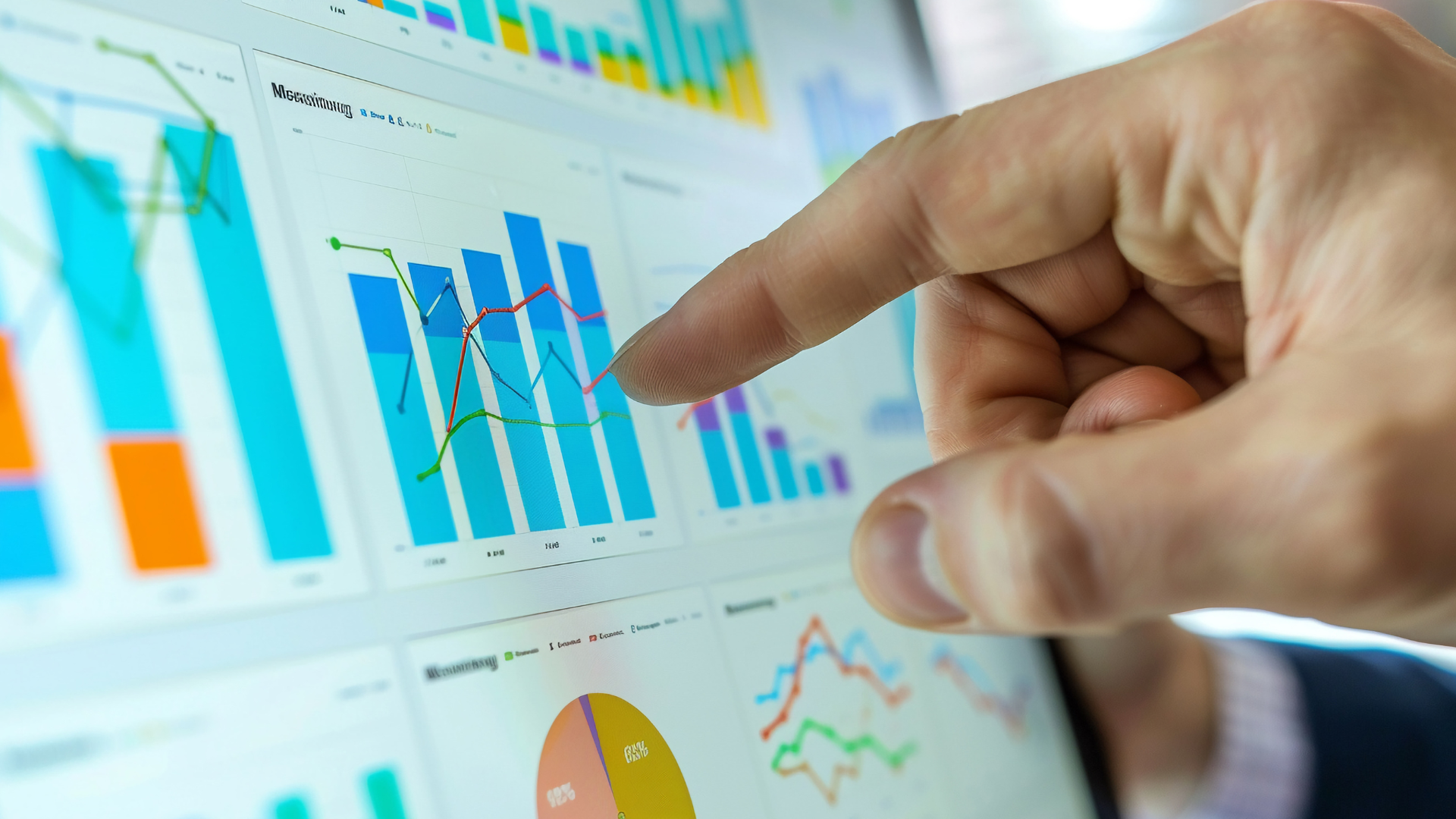 Hand pointing at colorful bar charts and graphs on a computer dashboard