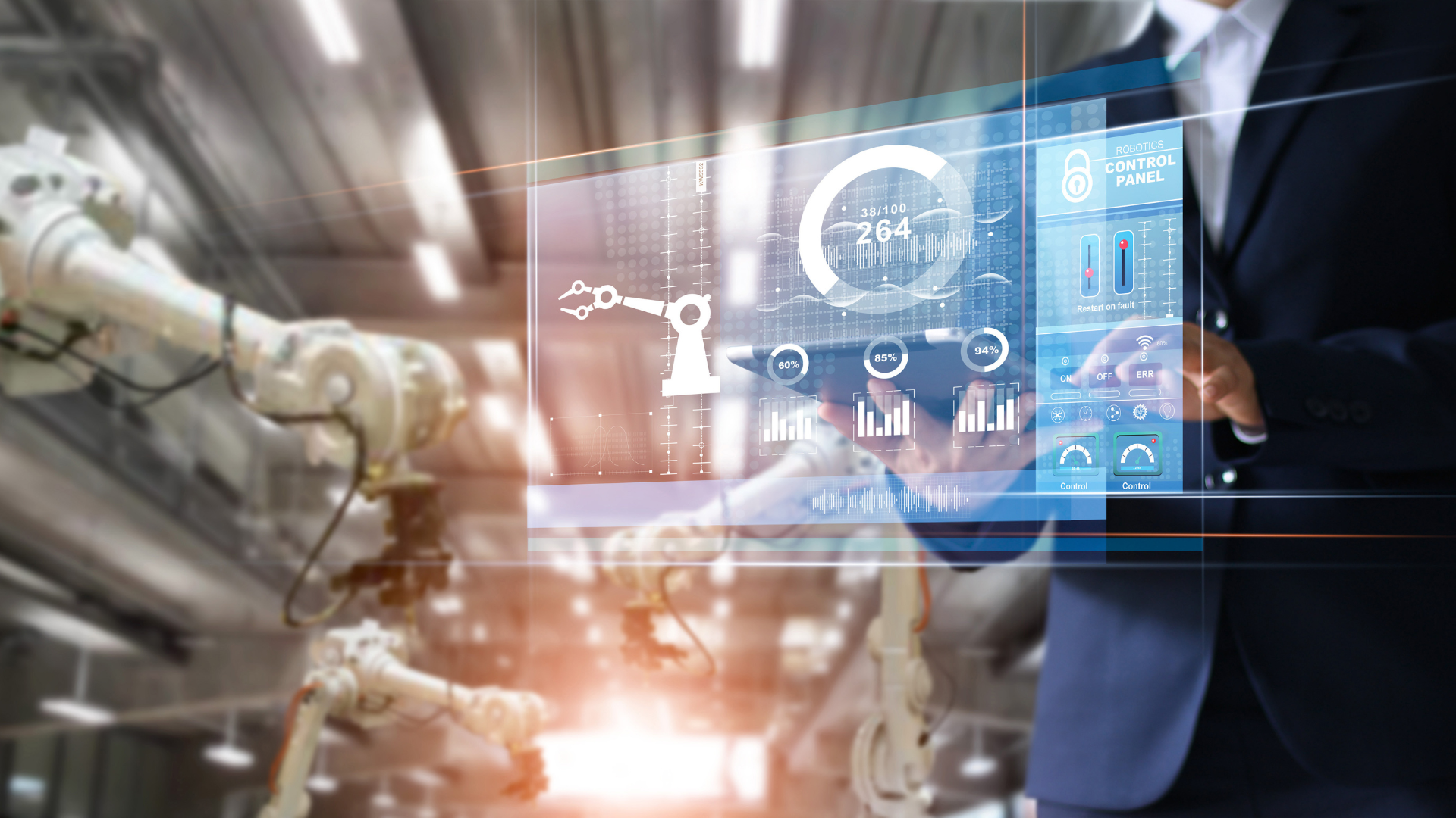 A man in a suit is holding a tablet in front of a robotic arm in a factory.
