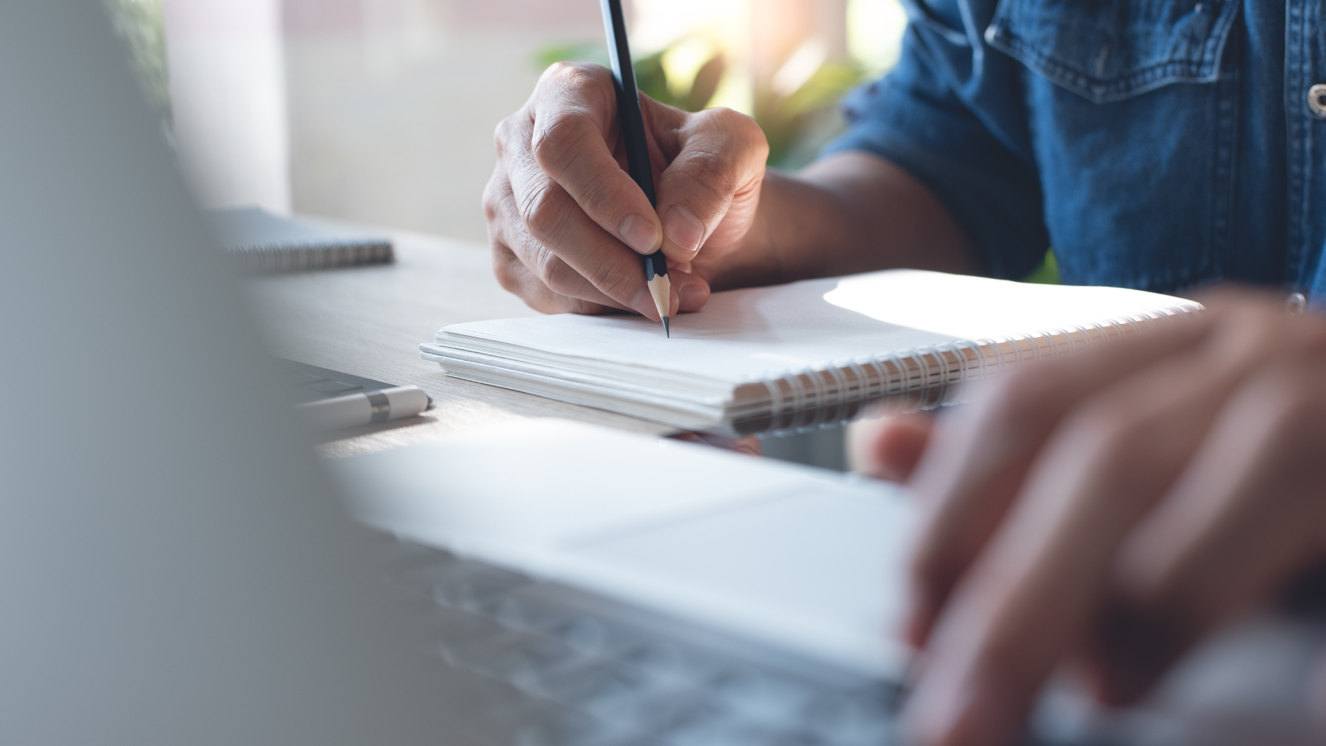 A person is writing in a notebook with a pencil.