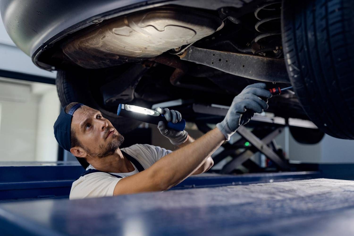 Man in protective gear sanding a car door in a body shop.