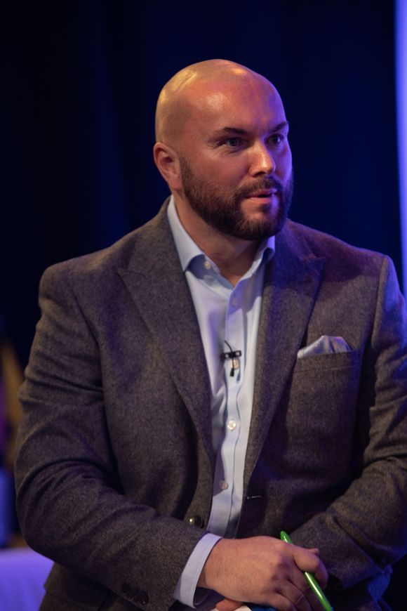 A bald man with a beard is wearing a suit and holding a microphone.