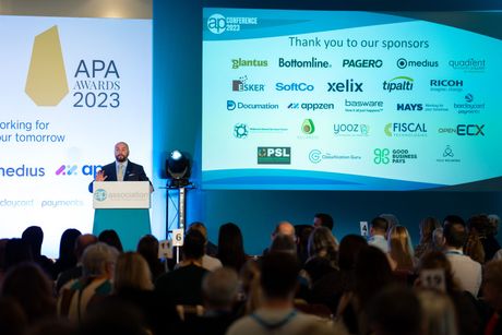 A man is giving a speech in front of a crowd at an apa awards event.