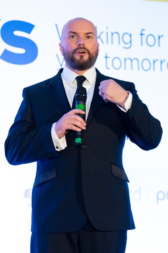 A bald man in a suit and tie is holding a microphone