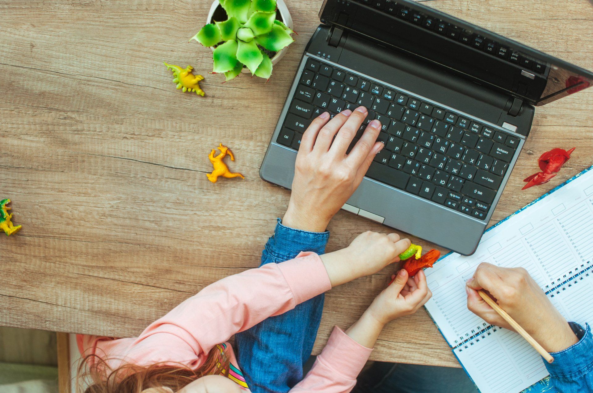A woman is typing on a laptop computer while a child writes in a notebook.